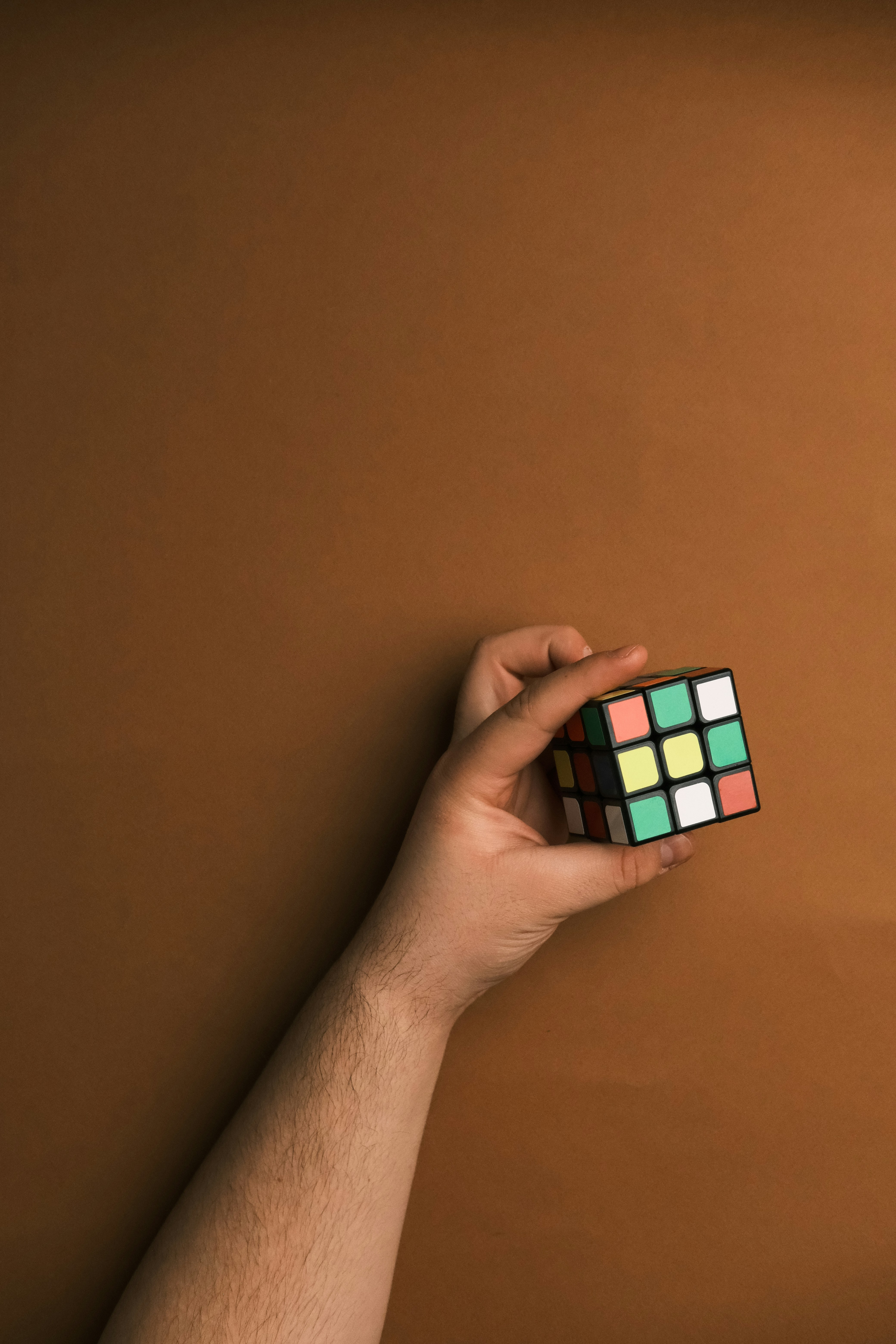 A hand holding a rubik cube on a brown background