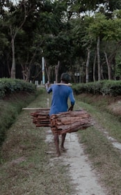A man carrying a large log down a dirt road
