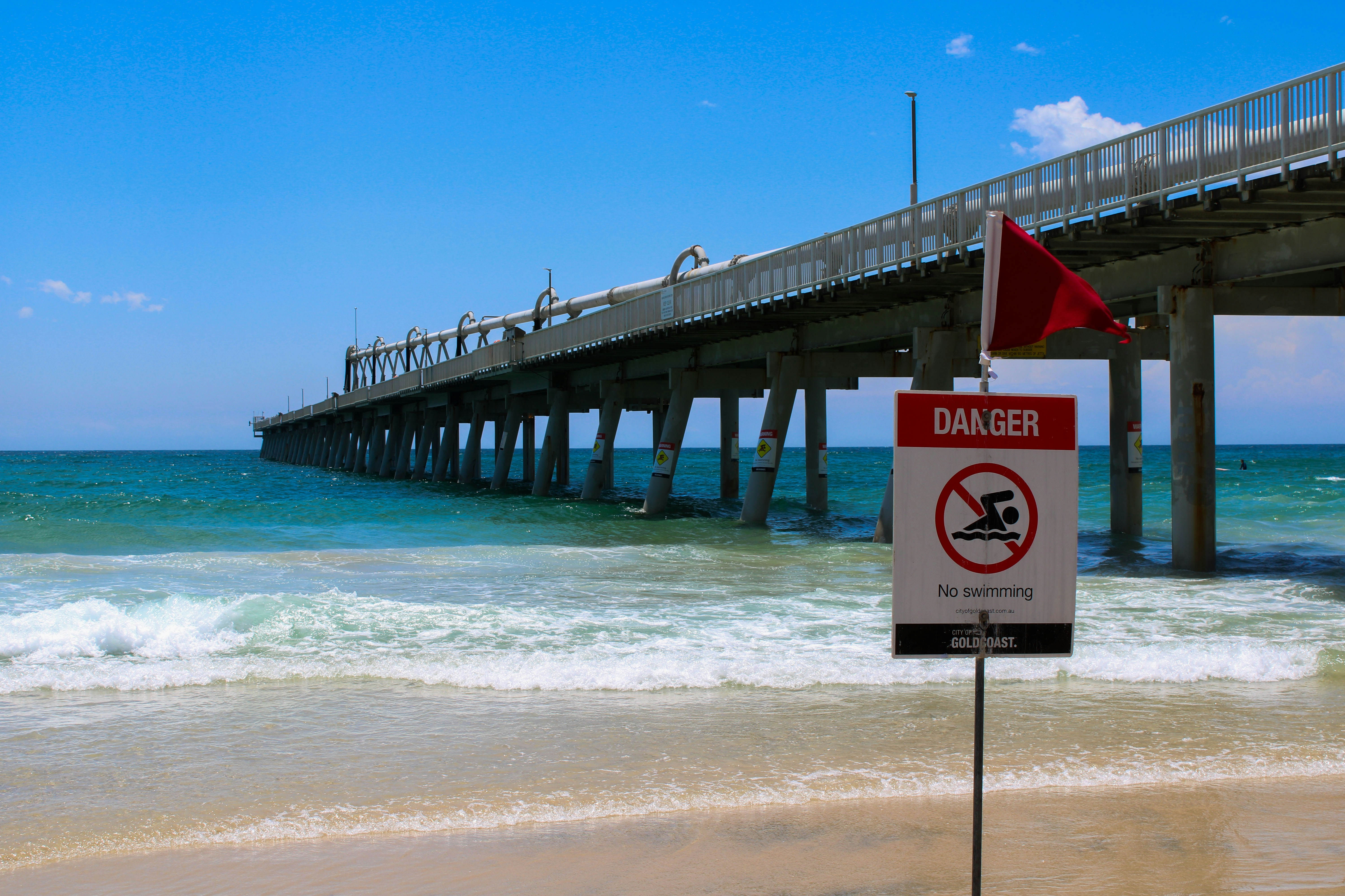 A no swimming sign on a beach near a pier