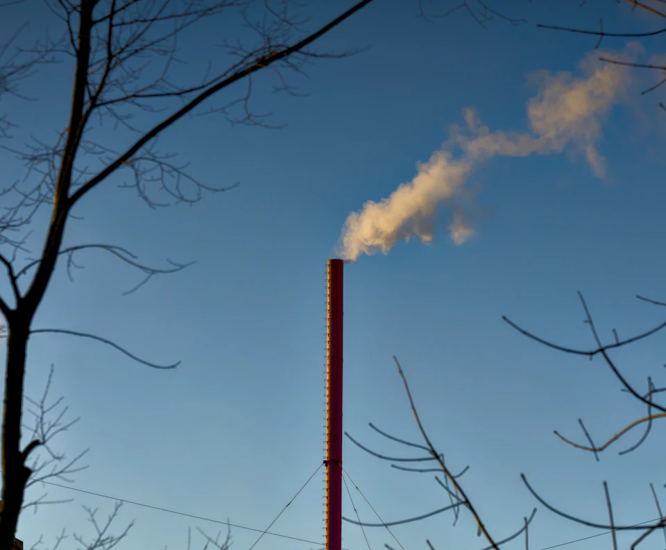 Tall red and white striped chimney emitting smoke across a clear blue sky landscape