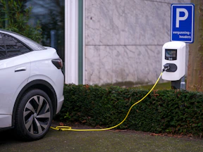 A white electric car plugged in to a parking meter