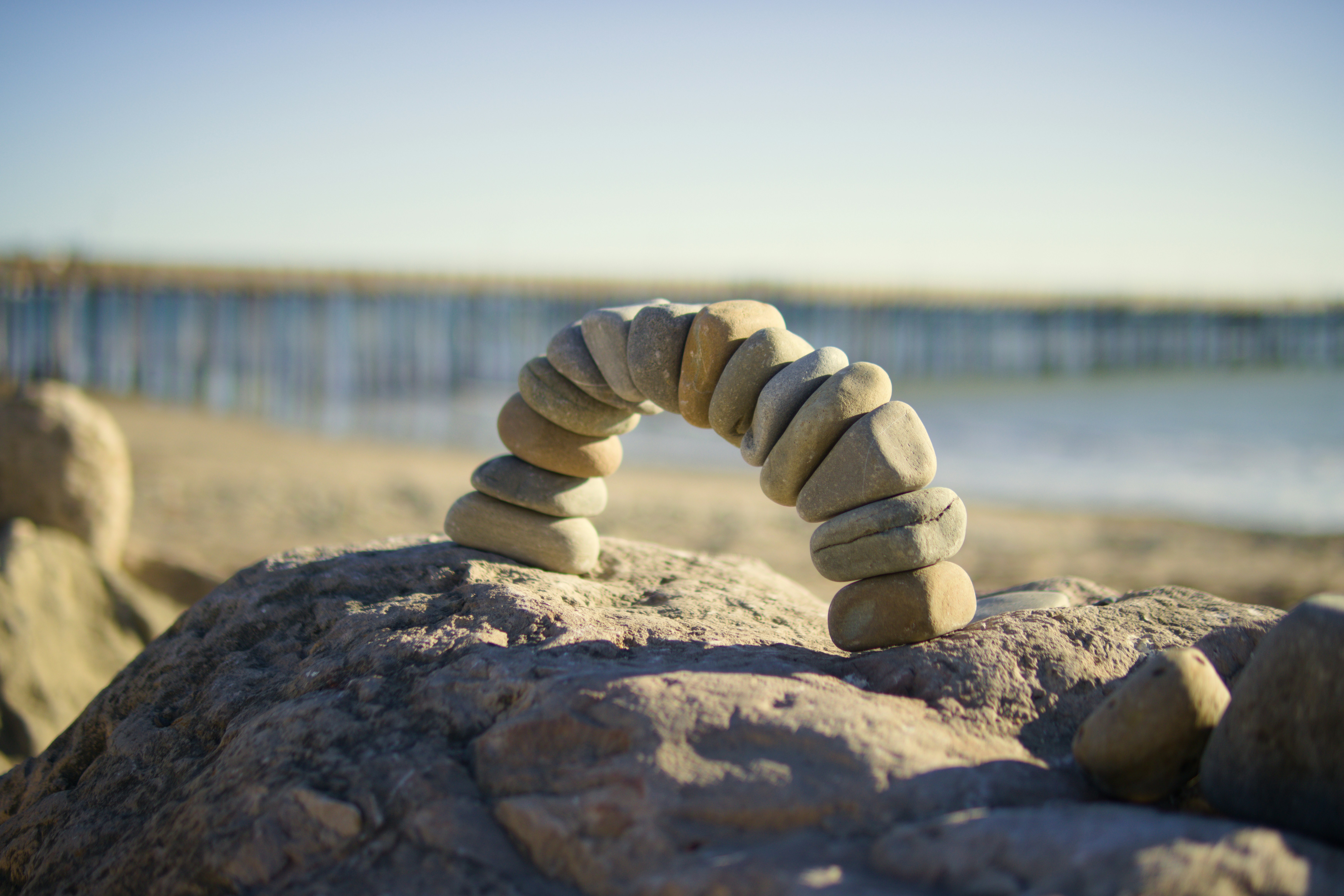 A rock formation on a beach with a pier in the background