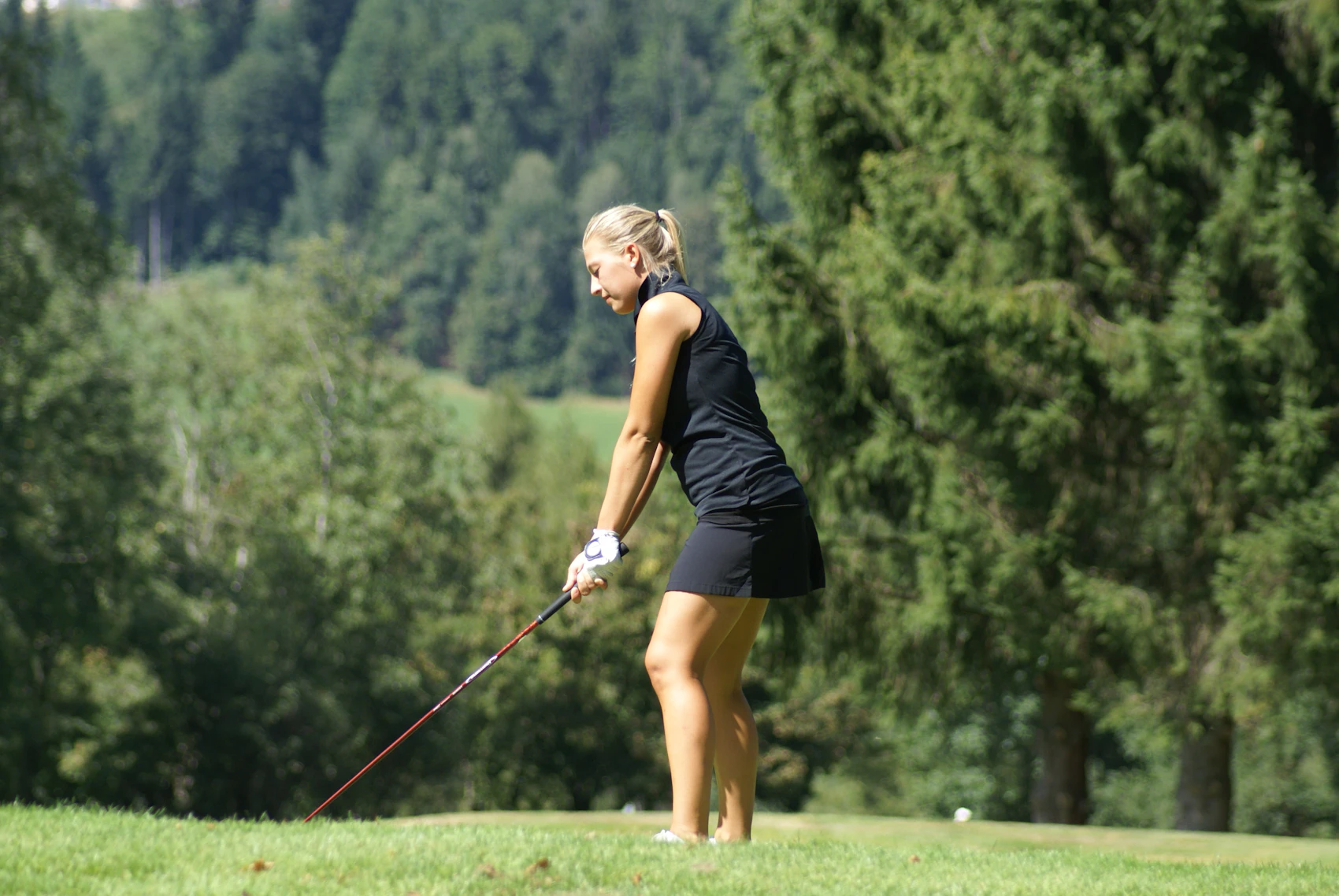 Woman preparing to play golf on a wooded course.