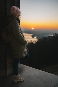 A person standing on a ledge looking at the sunset