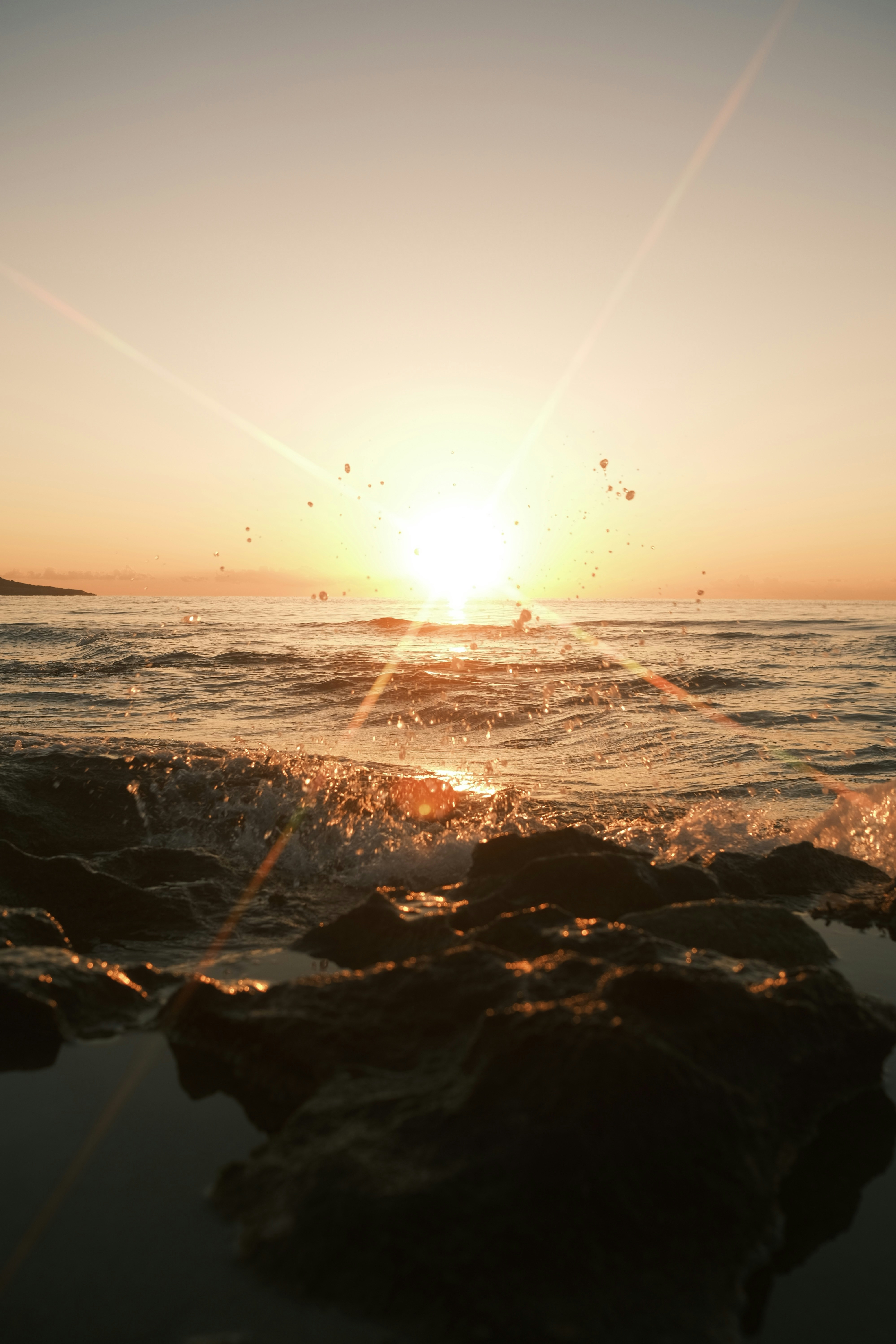 The sun is setting over the ocean with rocks in the foreground