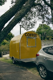A yellow coffee trailer parked next to a car