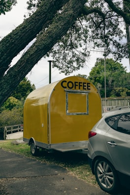 A yellow coffee trailer parked next to a car