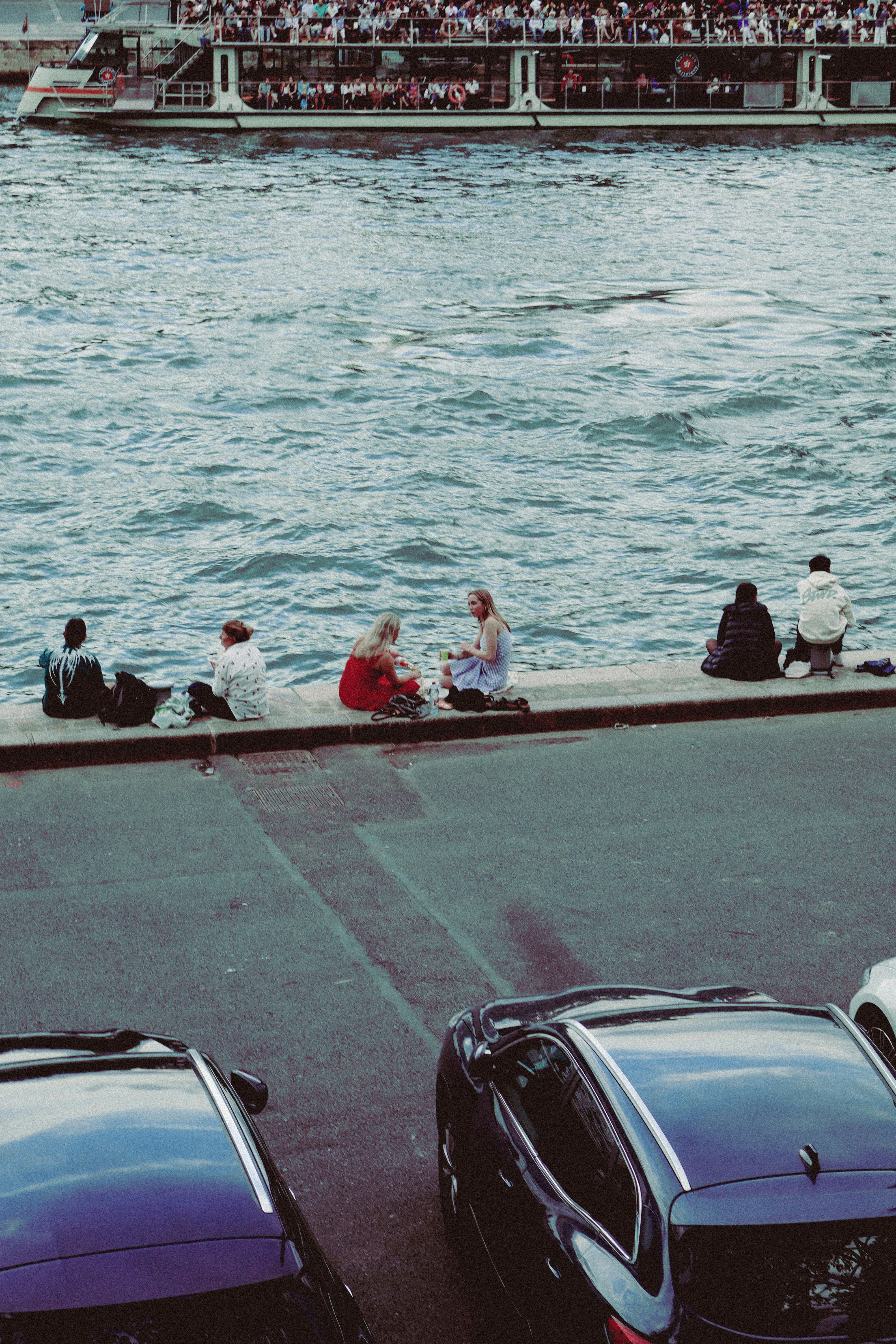 A group of people sitting on the side of a road next to a body of