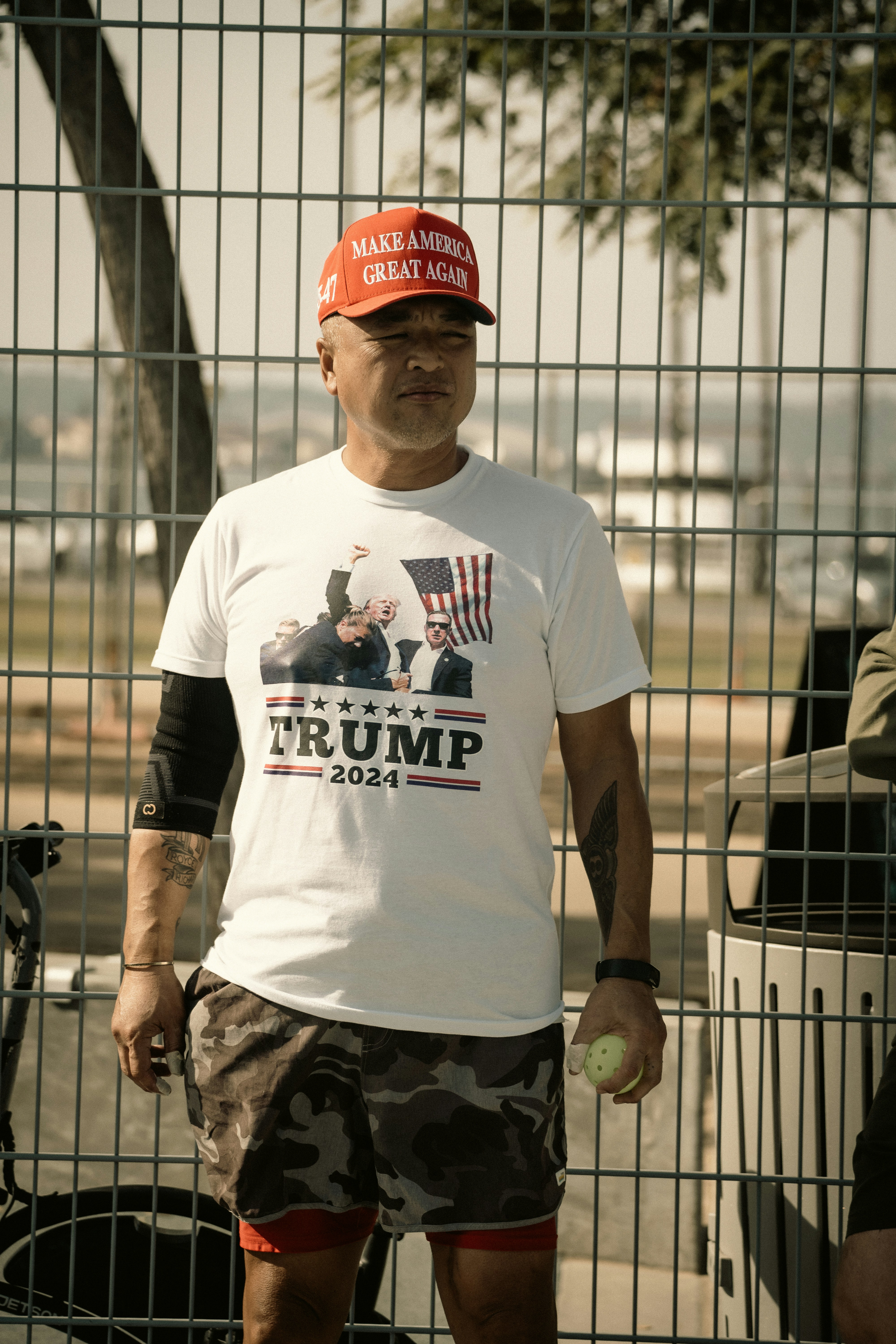 Un homme debout devant une clôture, tenant une balle de tennis