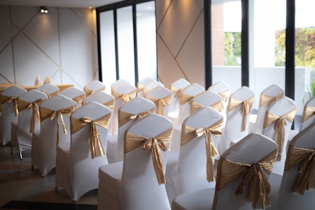 A room filled with white chairs covered in gold sashes