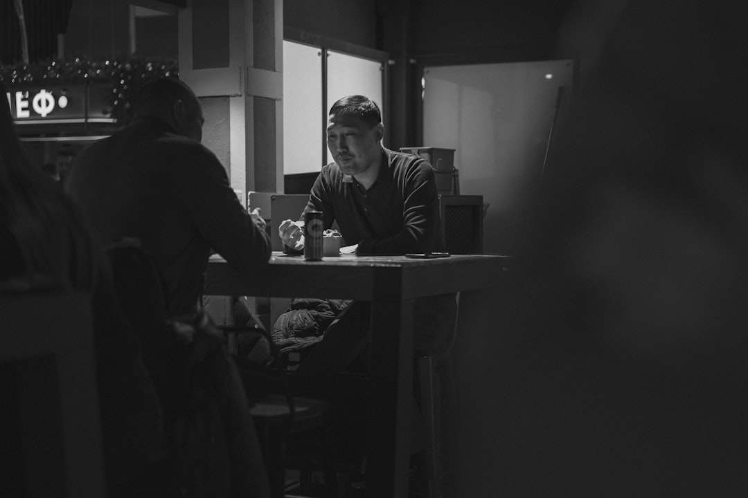A black and white photo of a man sitting at a table, Men talking at a table in a cafe