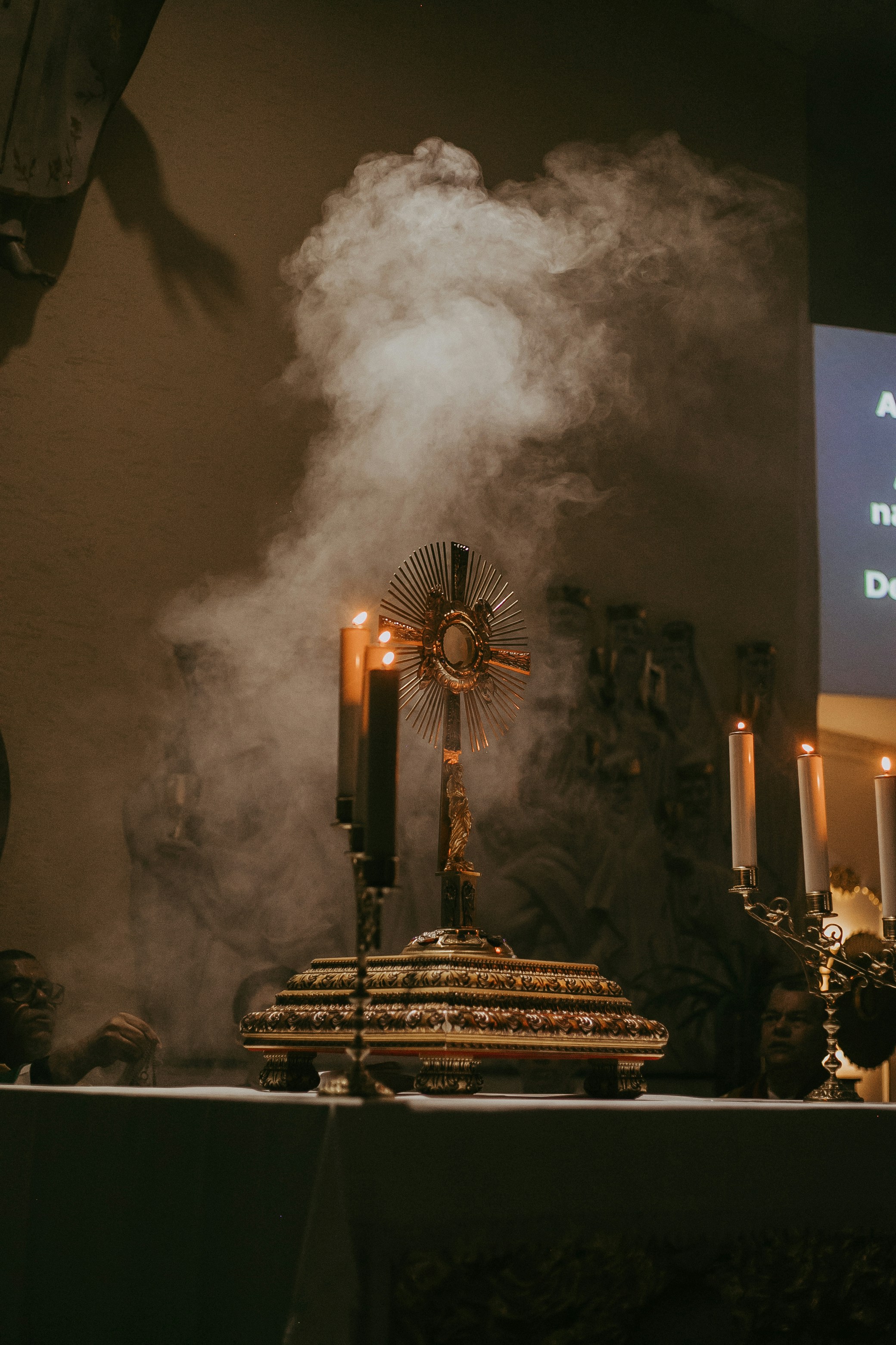 Un altar de iglesia con una cruz, velas y una pantalla de proyección.