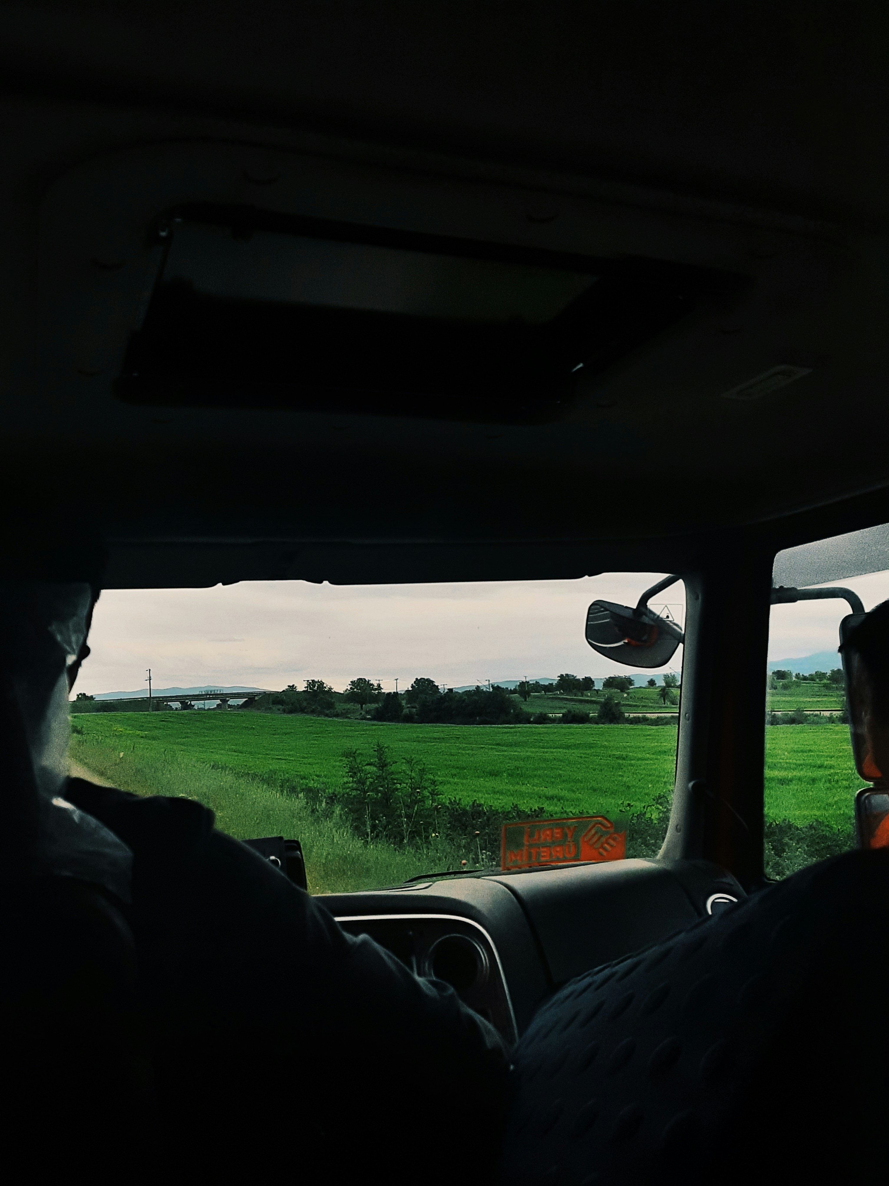A man driving a car down a road next to a lush green field