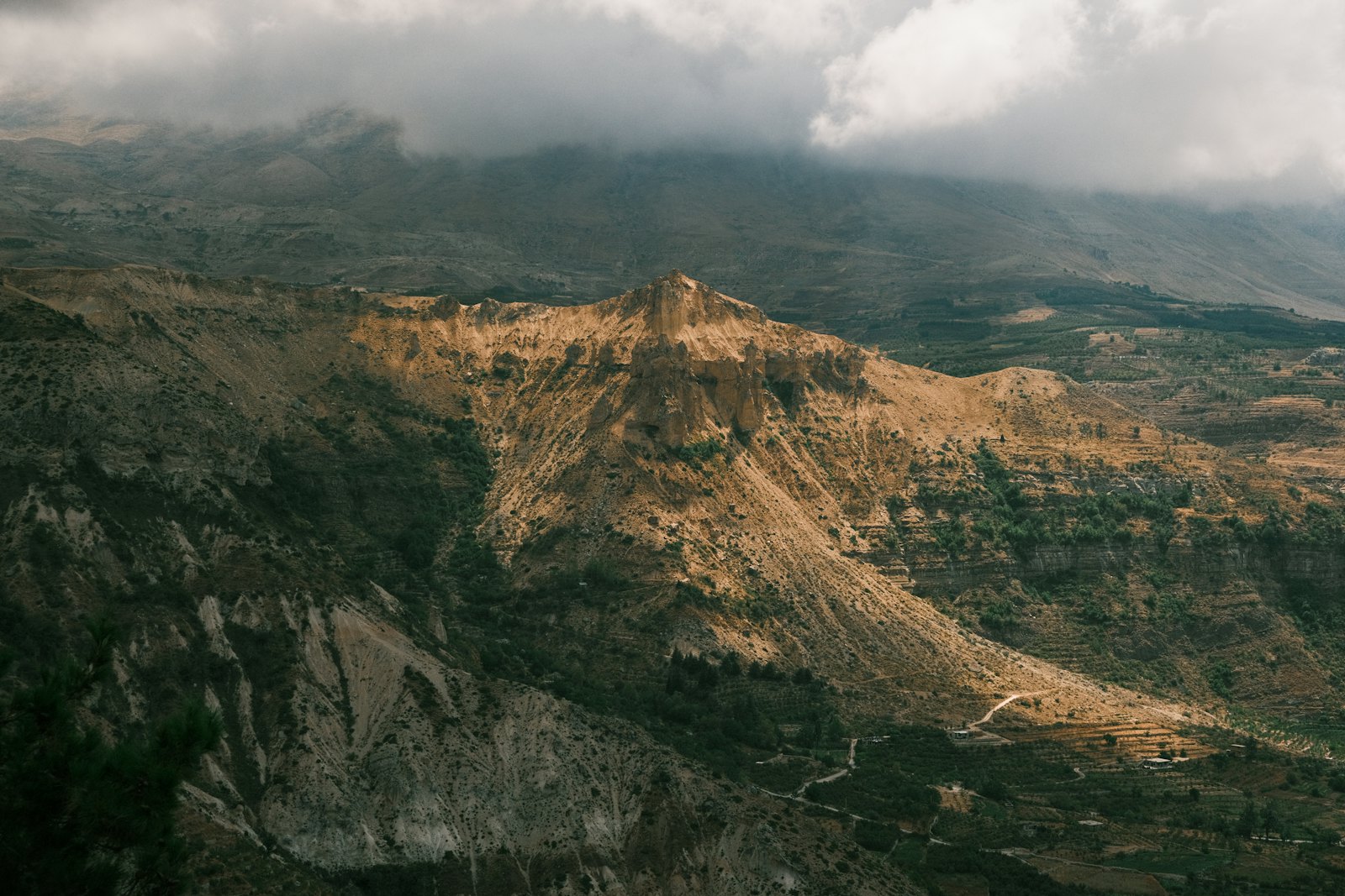 Sunlit mountain escarpment falling away into a deep green valley