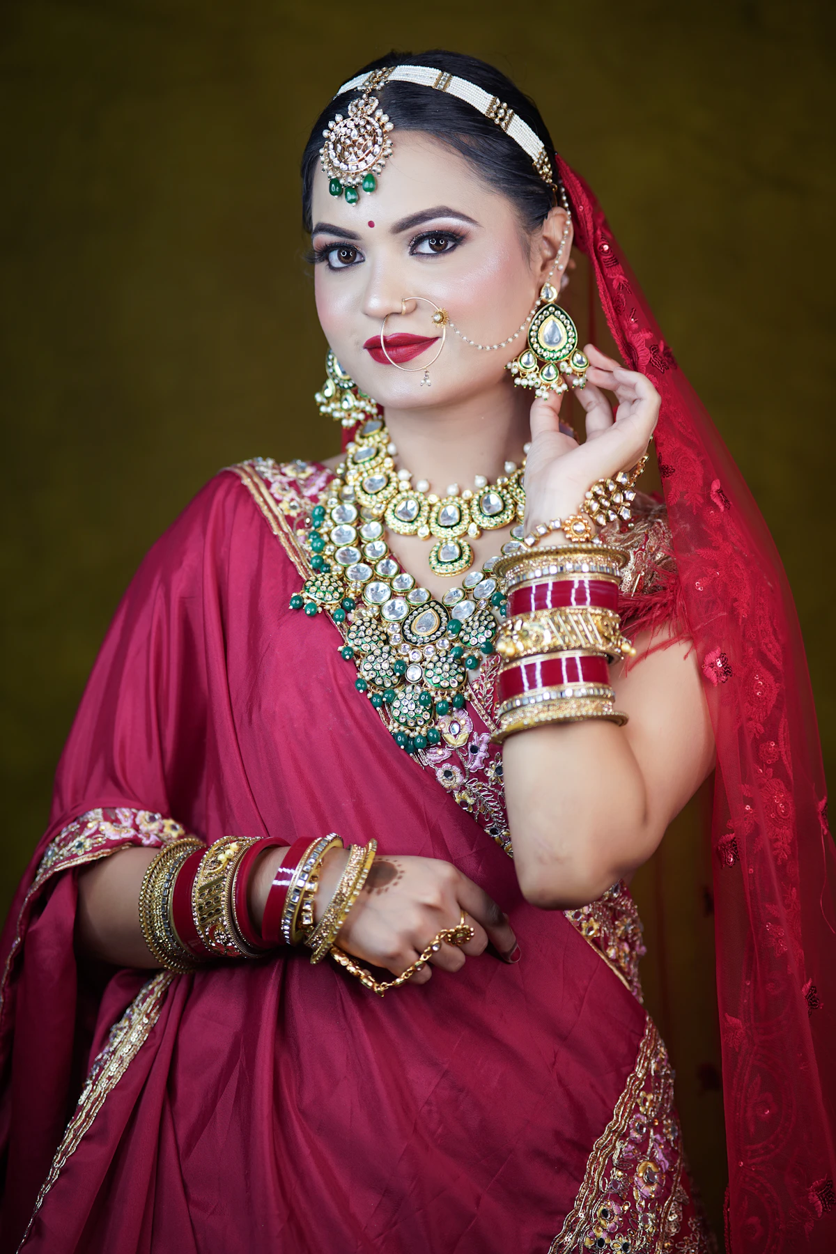 Indian bride in red wedding attire with layered jewelry and bangles