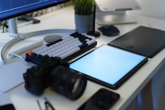 A desk with a computer, tablet and a camera