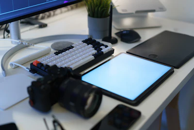 A desk with a computer, tablet and a camera