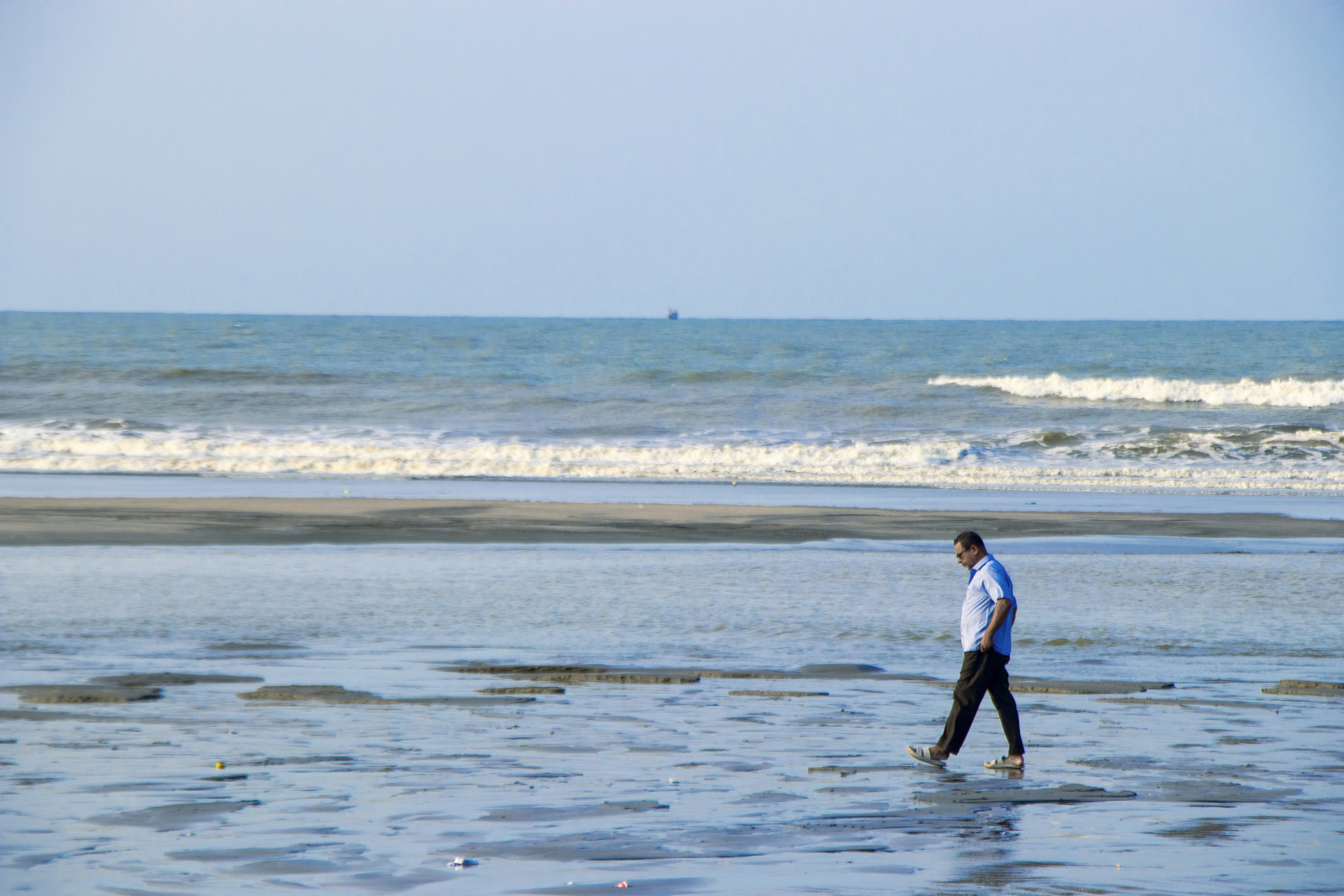 A man walking alone along the water on the immense sandy beach under the sun