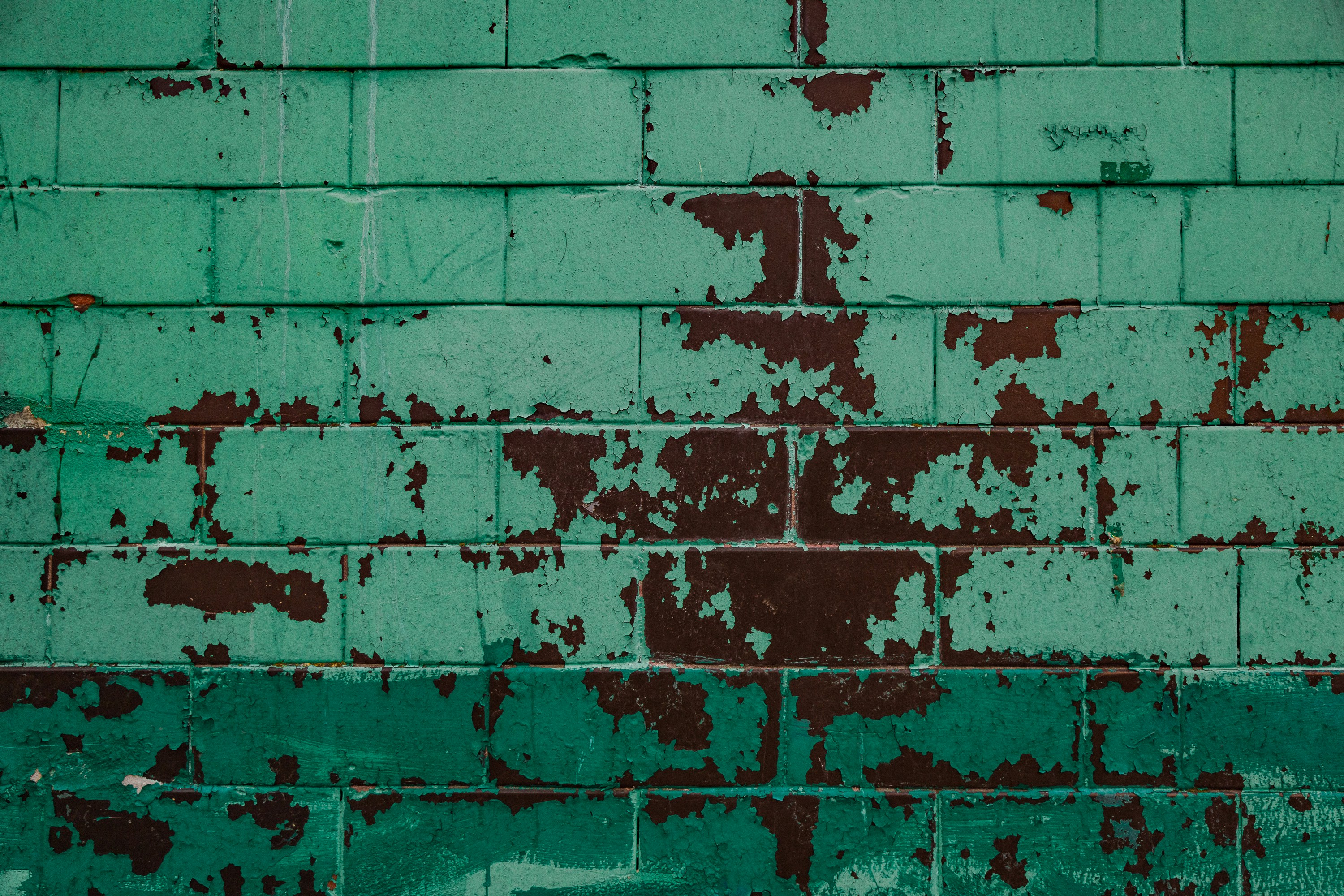 A green brick wall with rusted paint on it