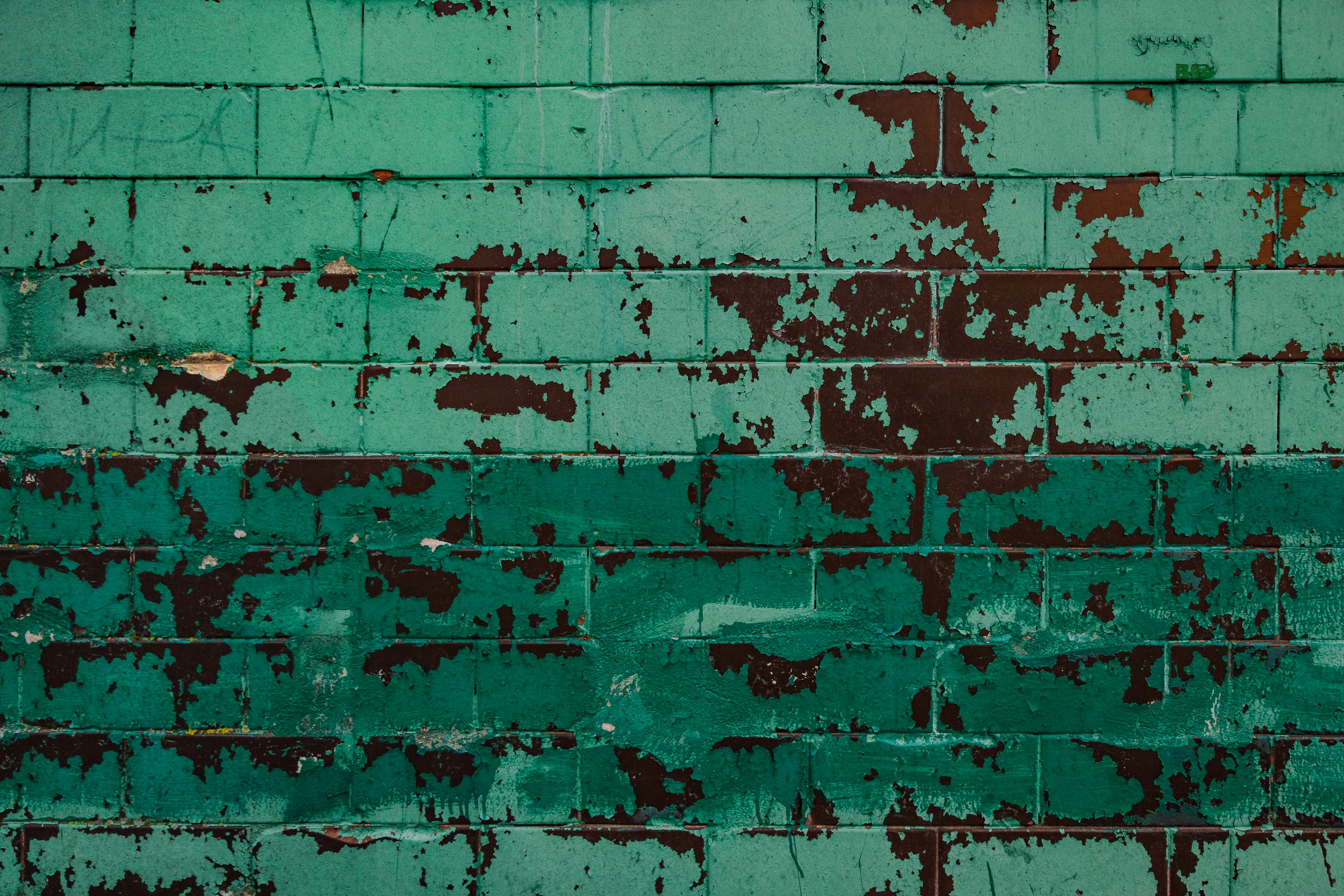 A green brick wall with peeling paint on it
