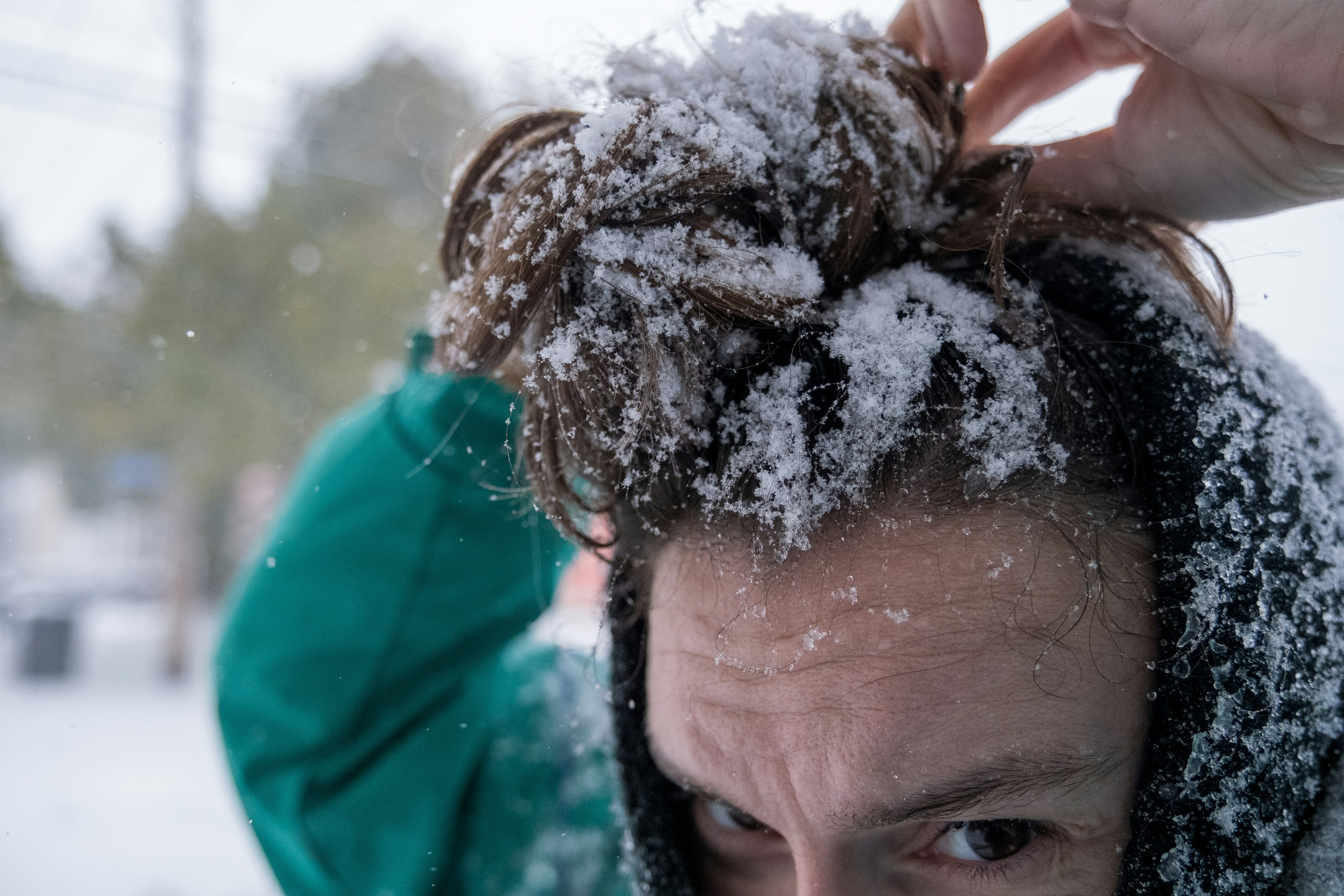 A man with his hair in a bun is covered in snow