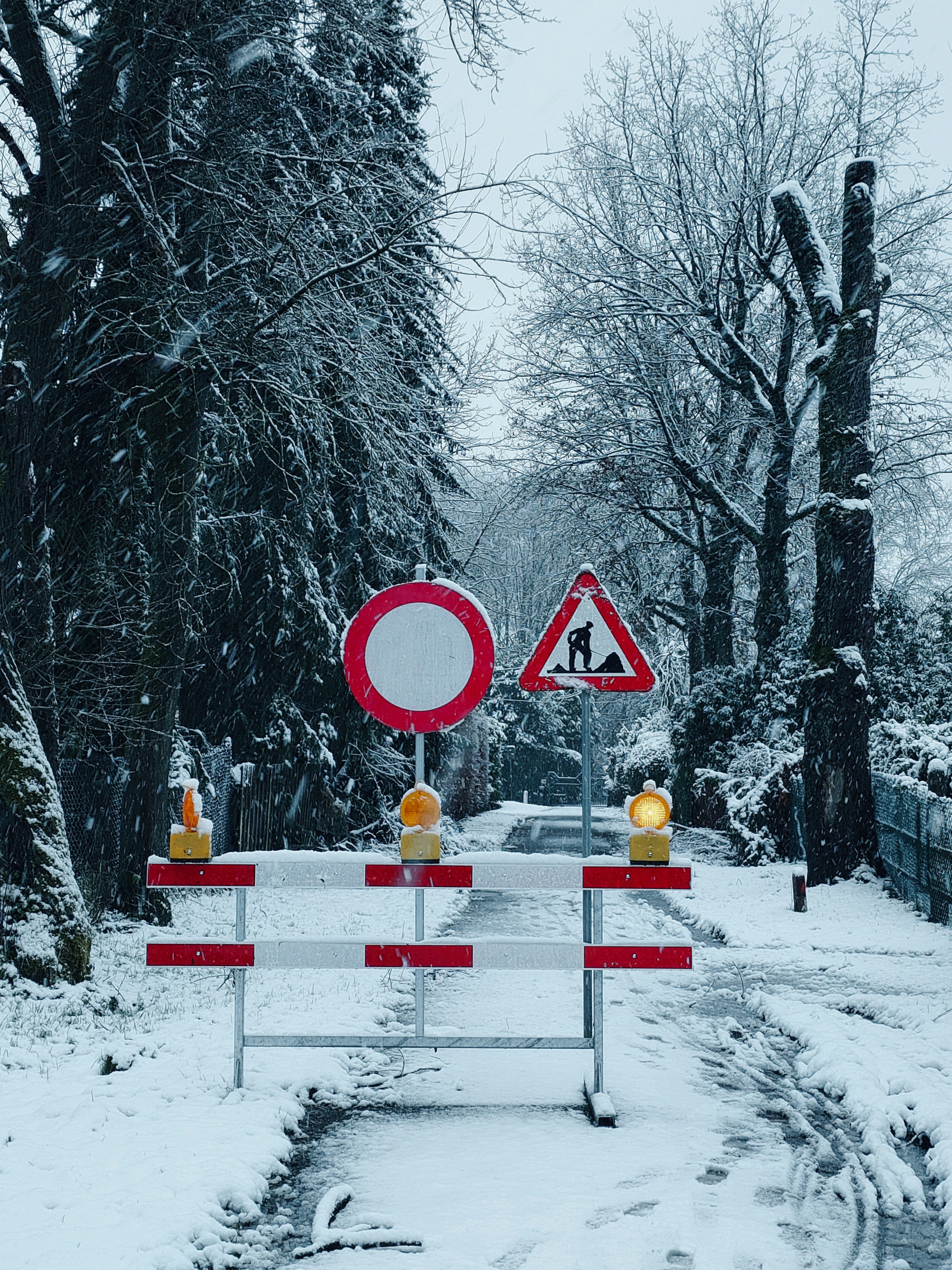 A red and white sign sitting on the side of a snow covered road