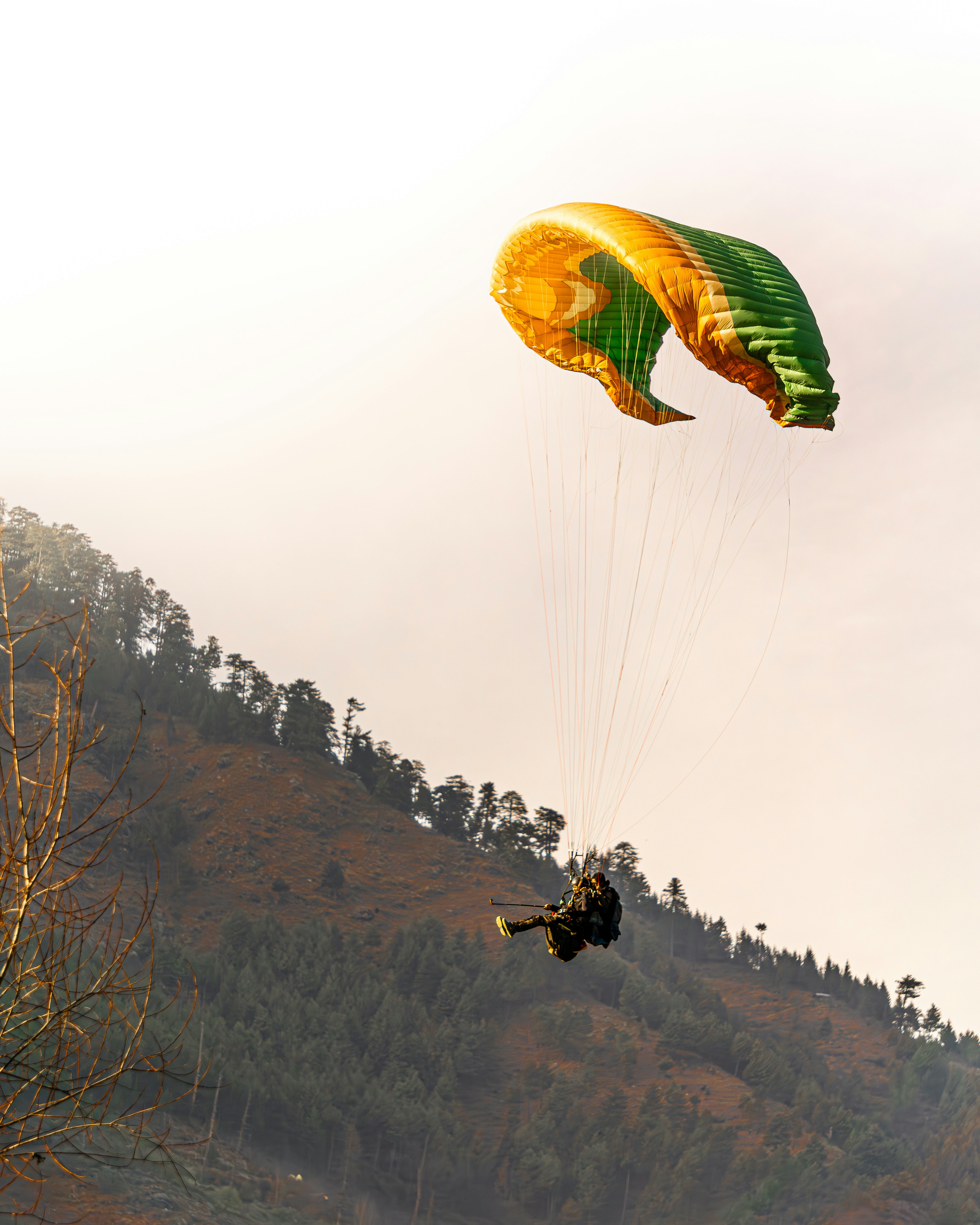 Two people are parasailing over a hill