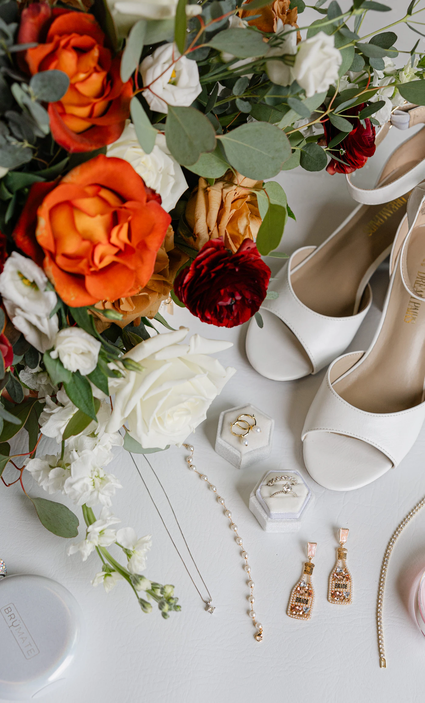 Wedding morning flatlay with a bouquet of flowers next to shoes and a wedding ring on a flat surface
