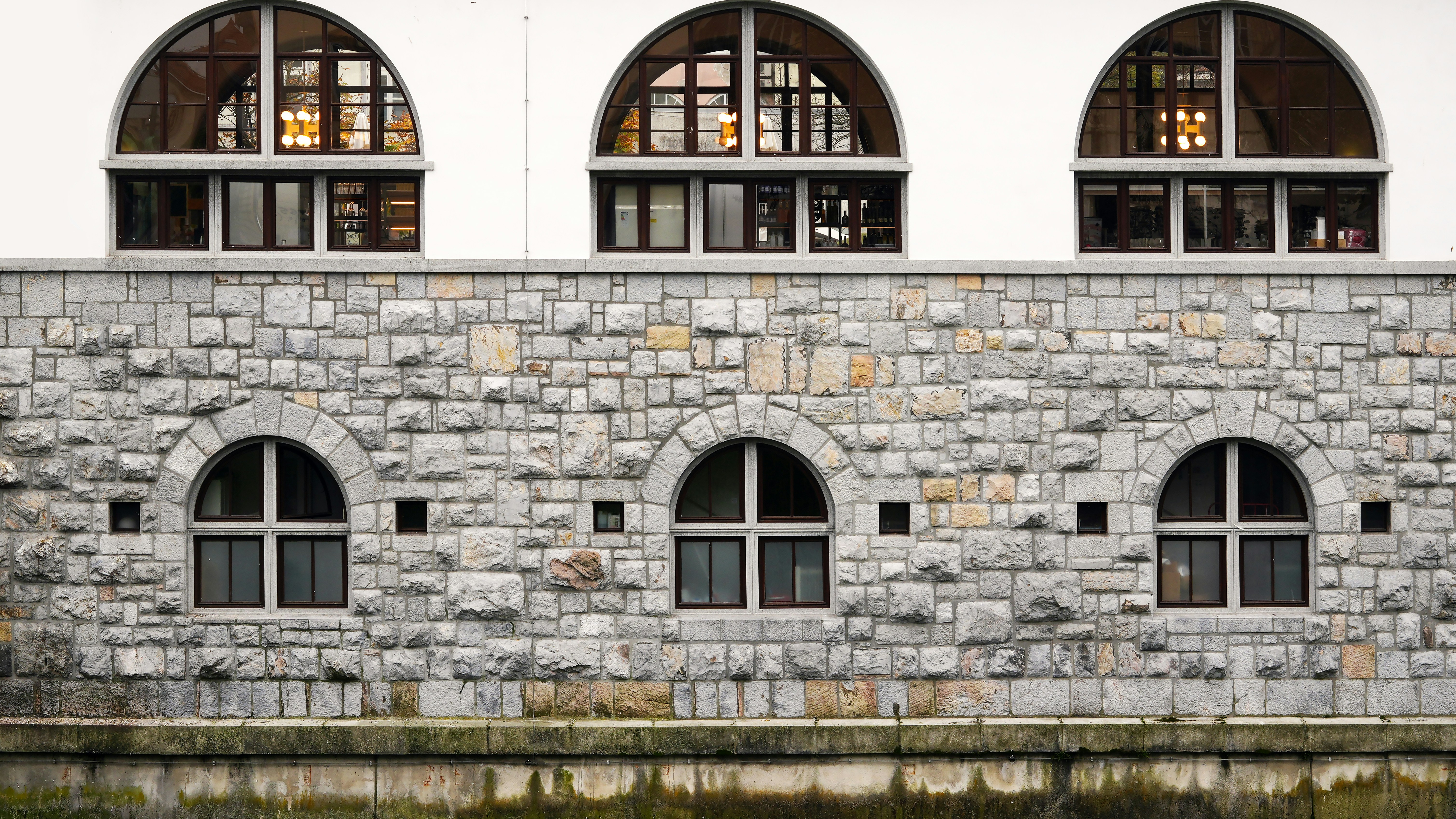 A stone building with arched windows next to a body of water