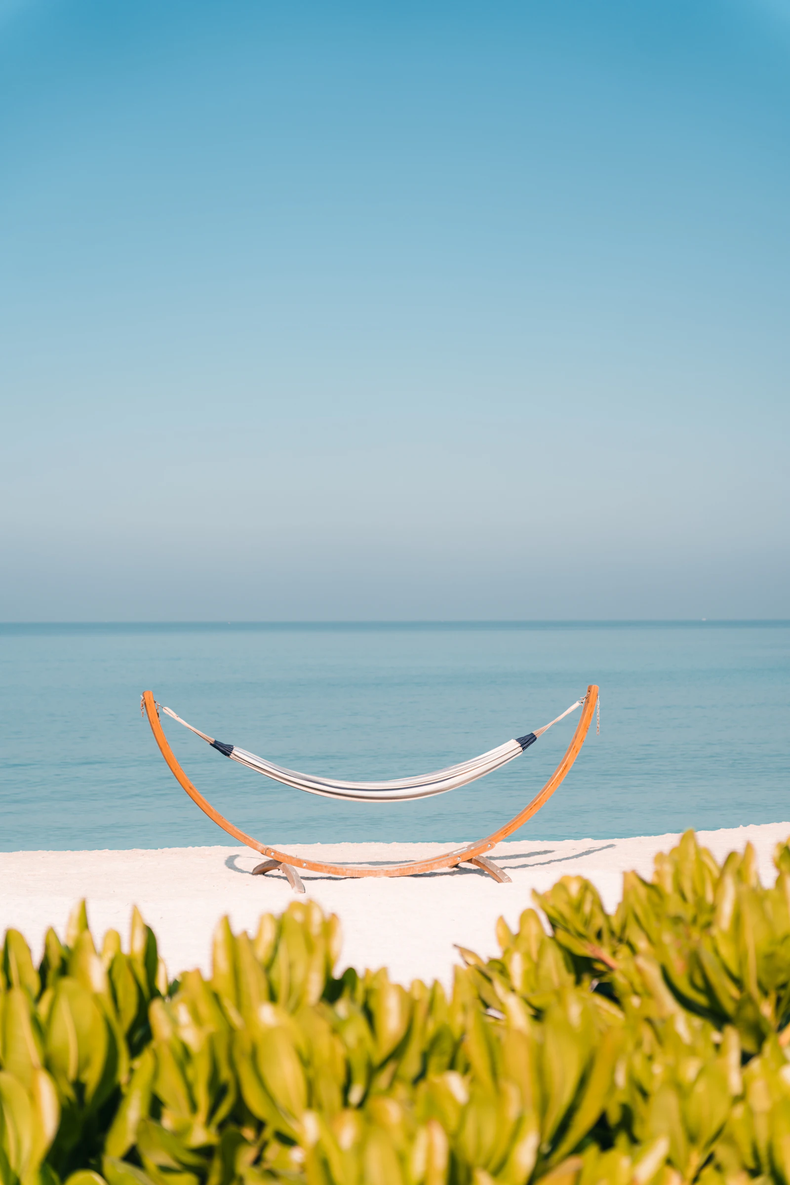 Empty hammock strung between palms on a quiet beach at dusk — the postcard image of early retirement that the withdrawal math is designed to fund.