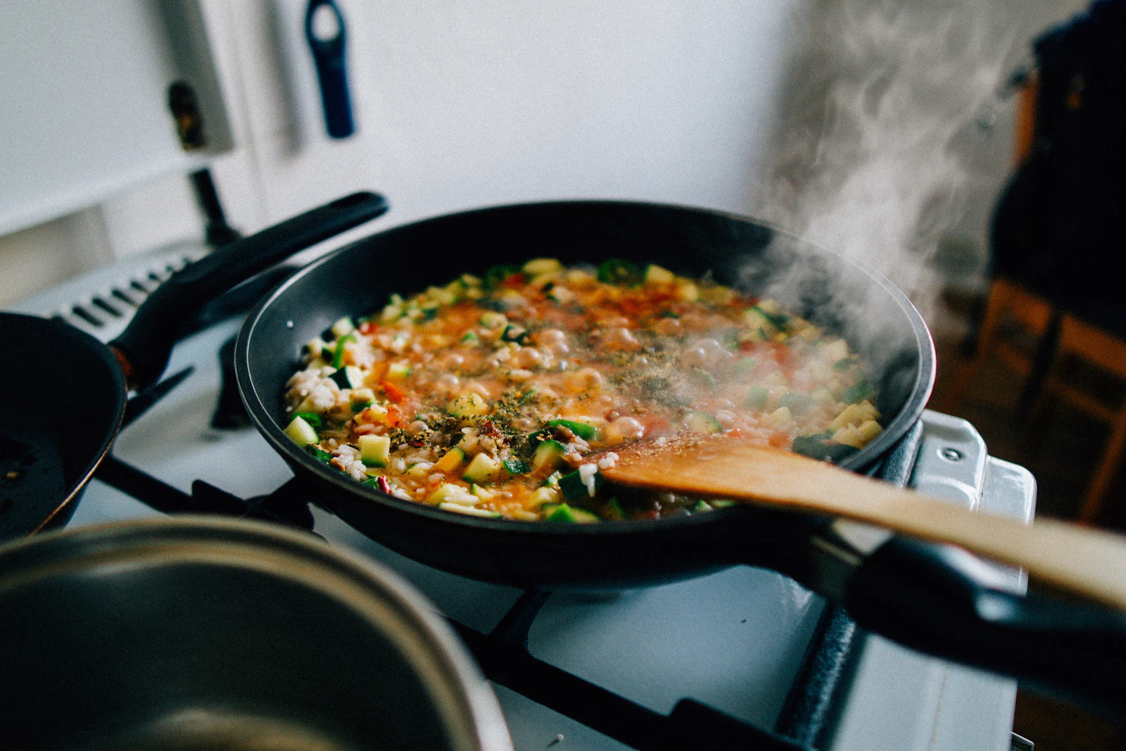 Vegetables cooking in a pan on the stove with a wooden spoon
