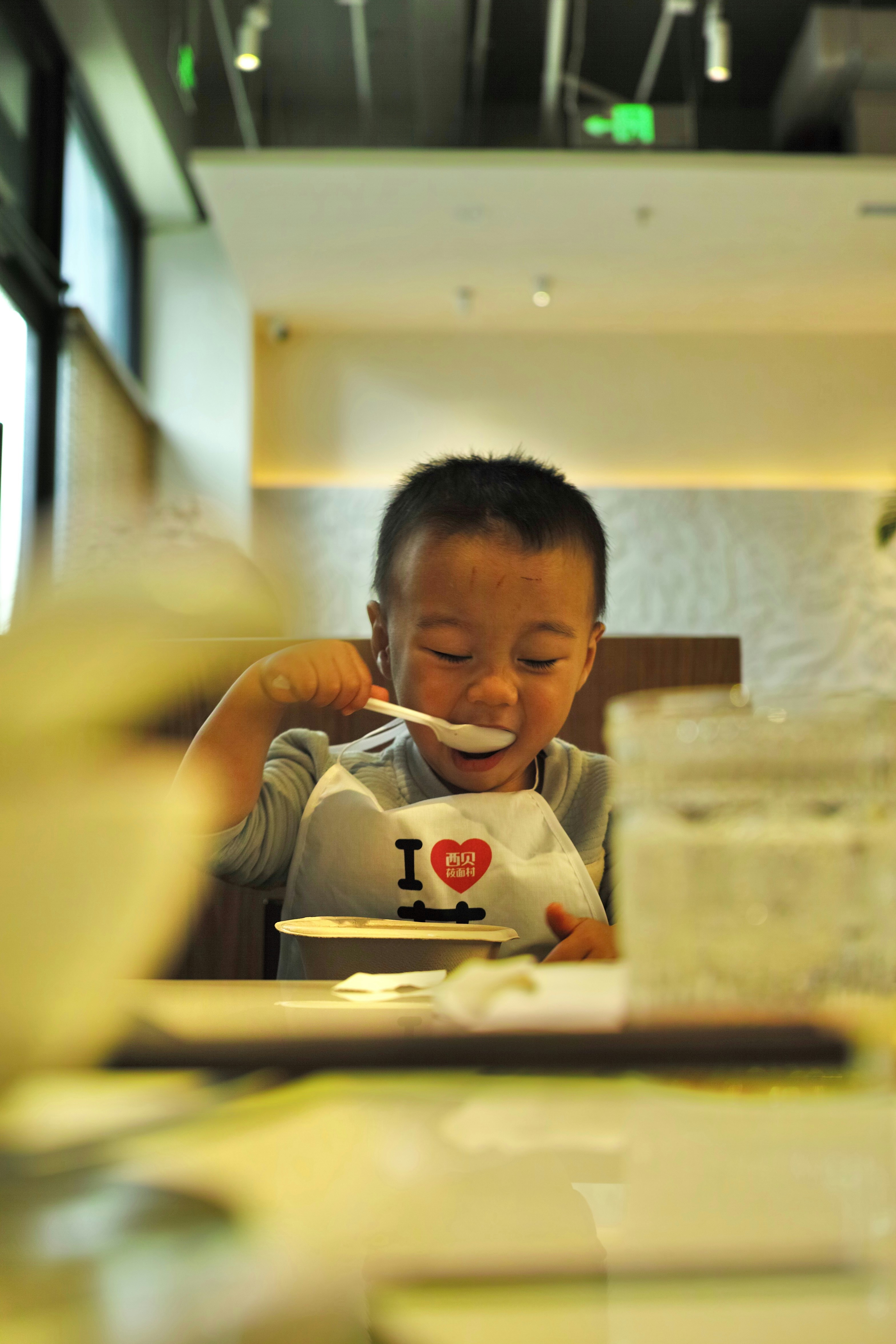 A young boy sitting at a table with a spoon in his mouth