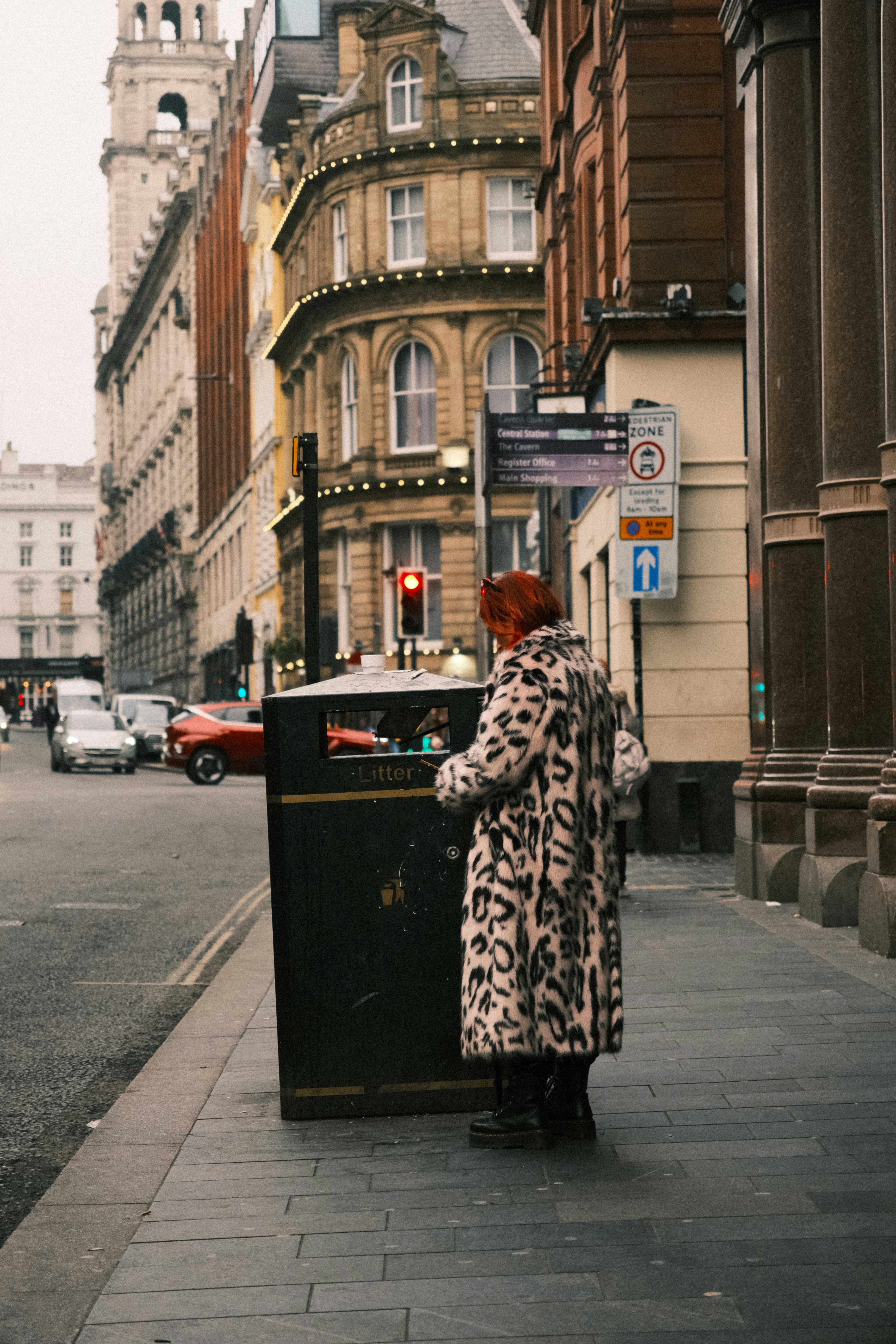 A woman standing on a sidewalk next to a trash can