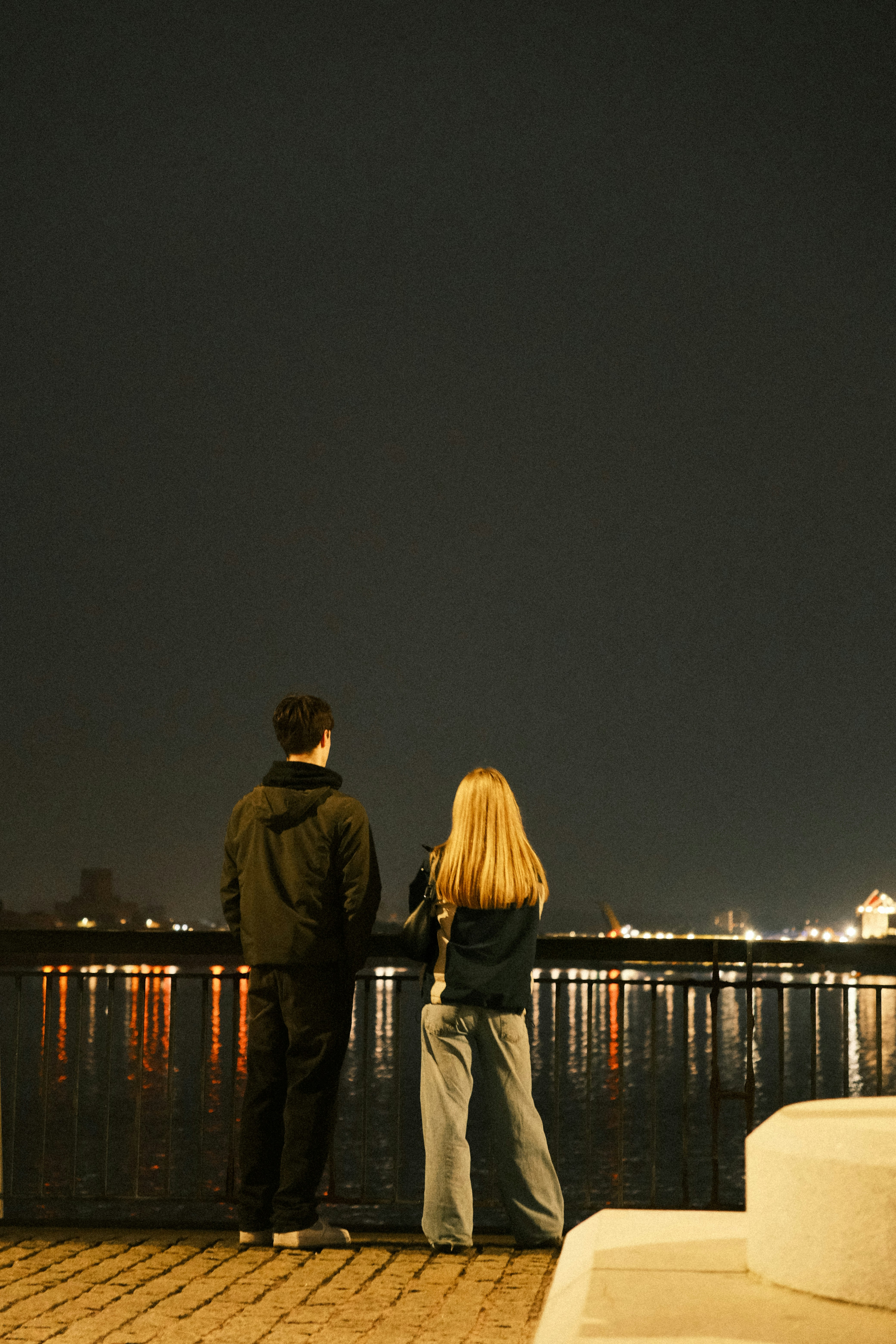 A man and a woman standing on a pier looking at the water