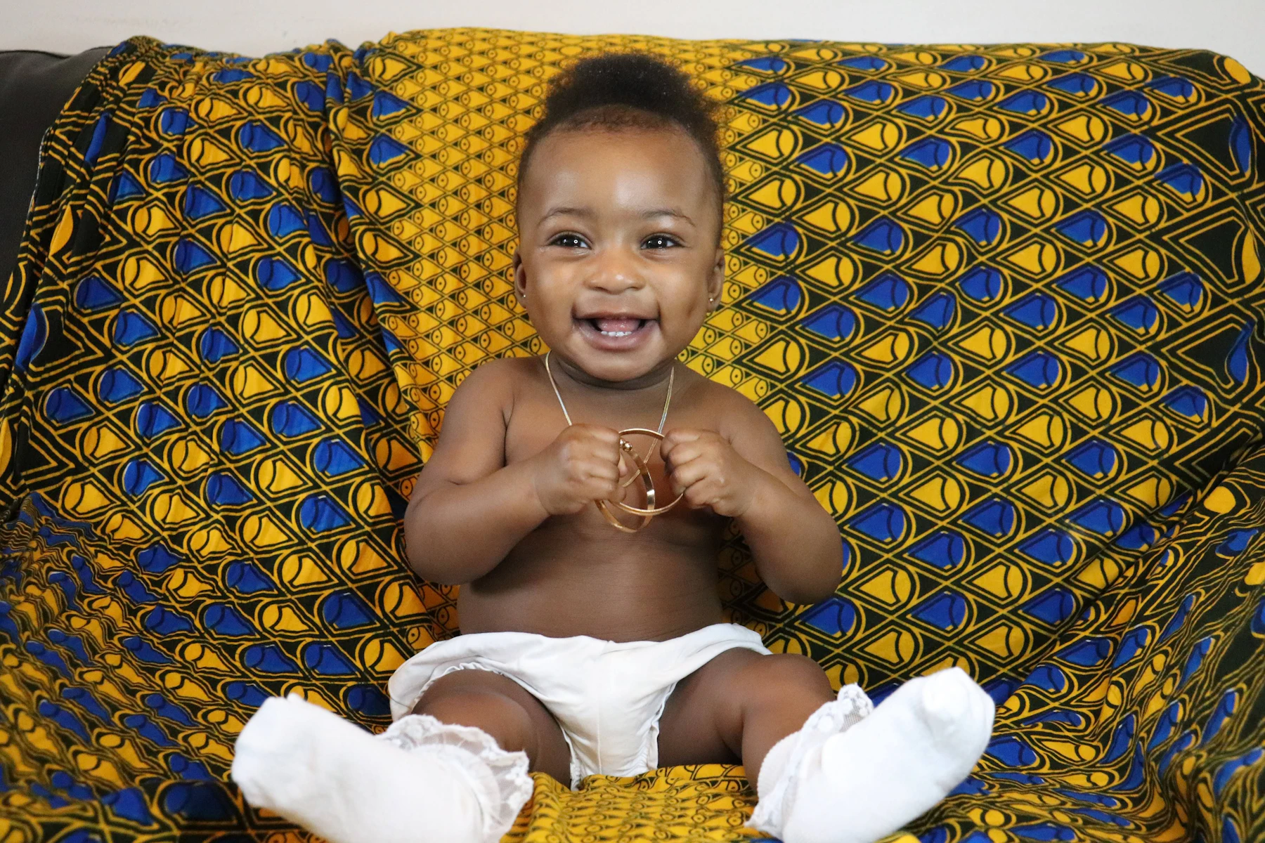 A smiling baby sitting on a colourful African print cloth