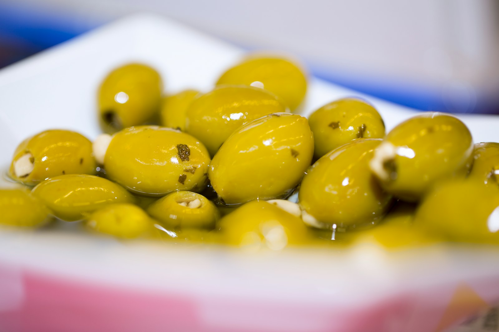 A white bowl of green olives with herbs and garlic
