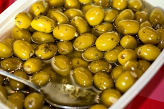 A container filled with green olives and a spoon