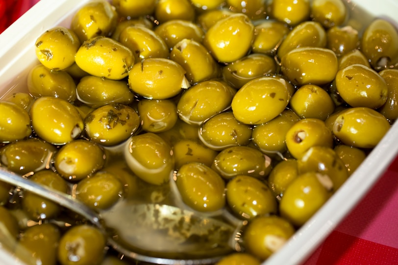 A container filled with green olives and a spoon