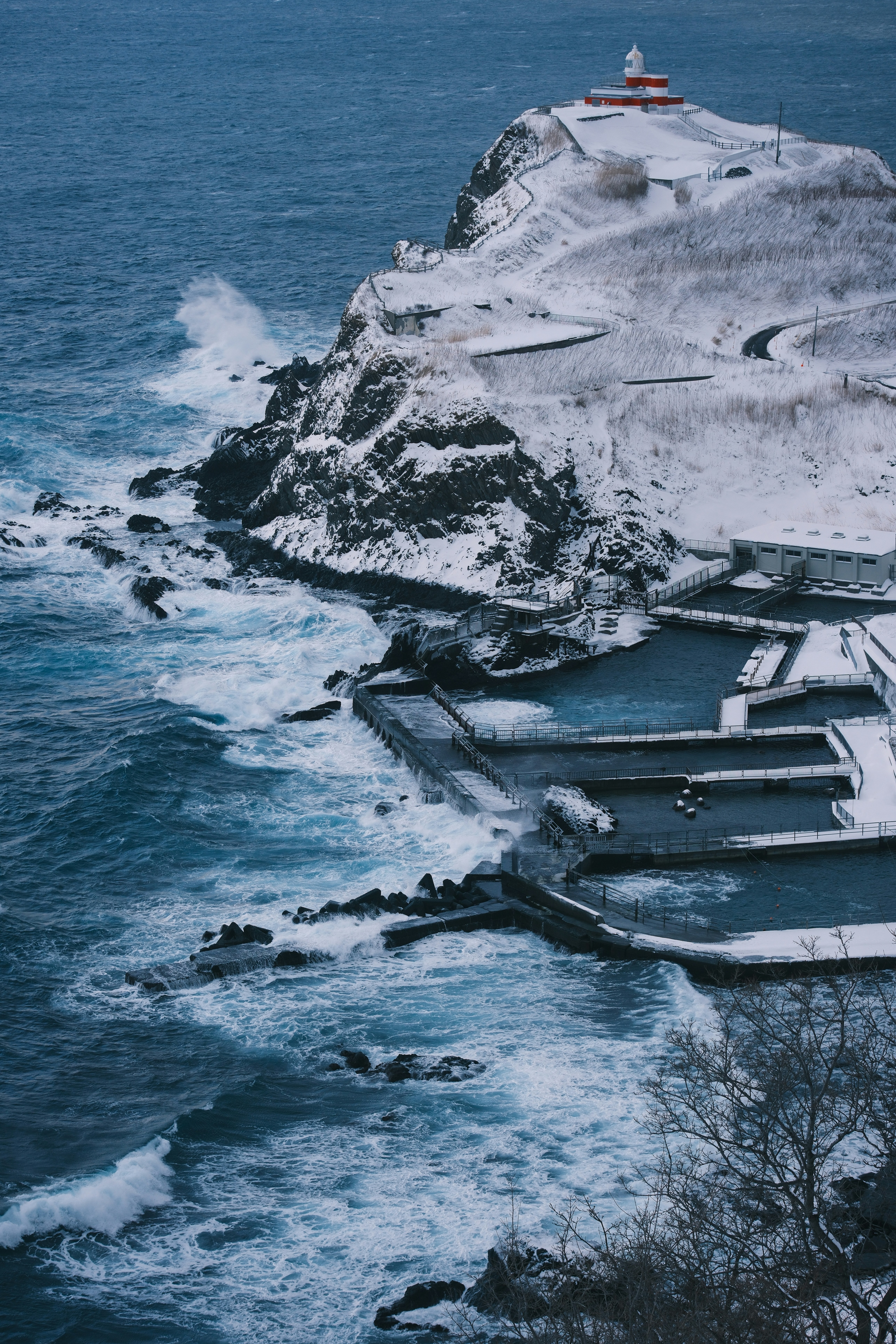 A lighthouse on top of a snowy hill next to the ocean