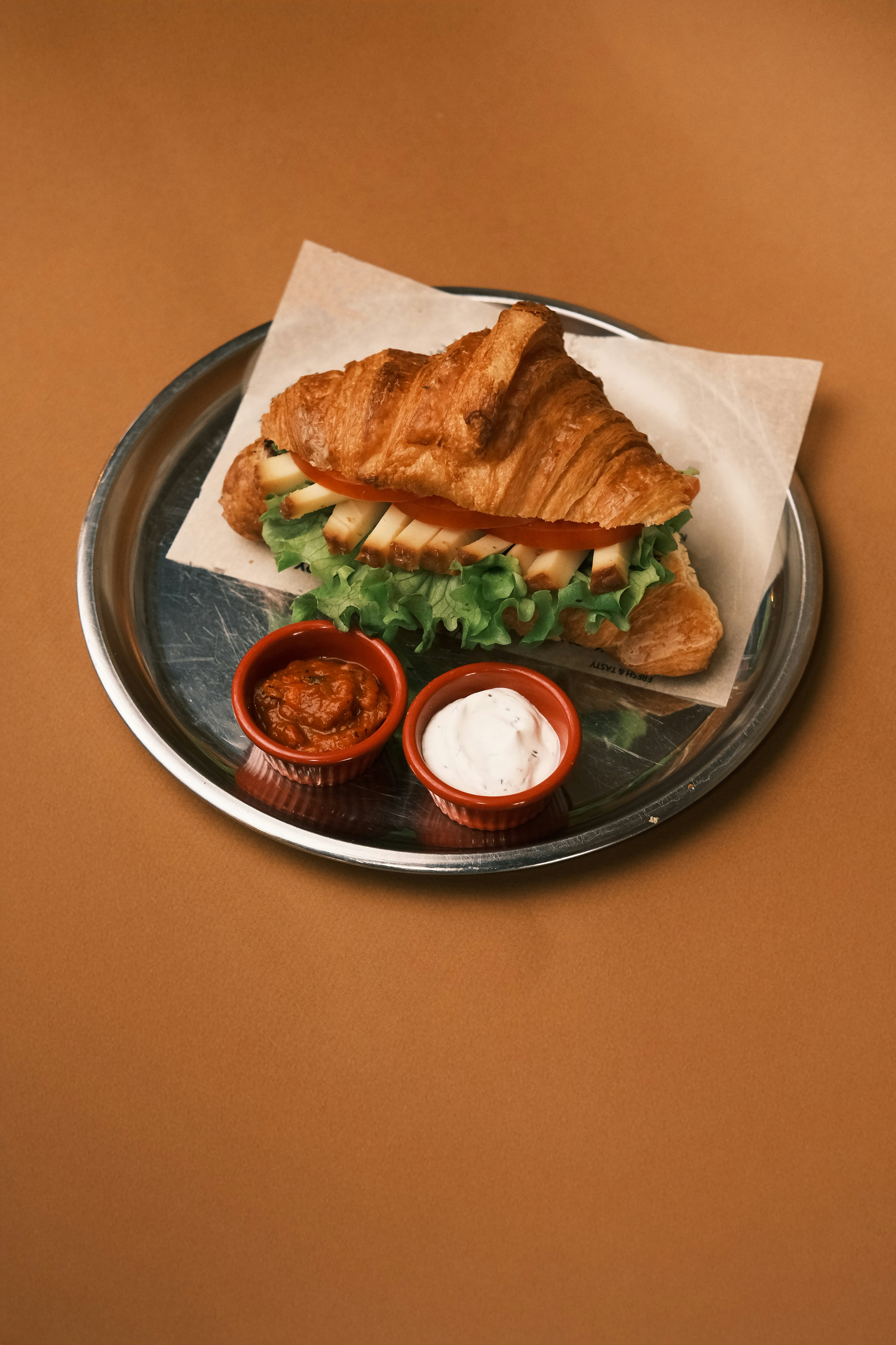 A croissant sandwich with lettuce and tomato sauce on a plate