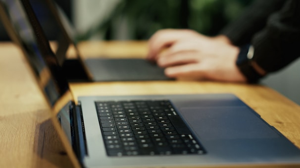 A person typing on a laptop on a wooden table