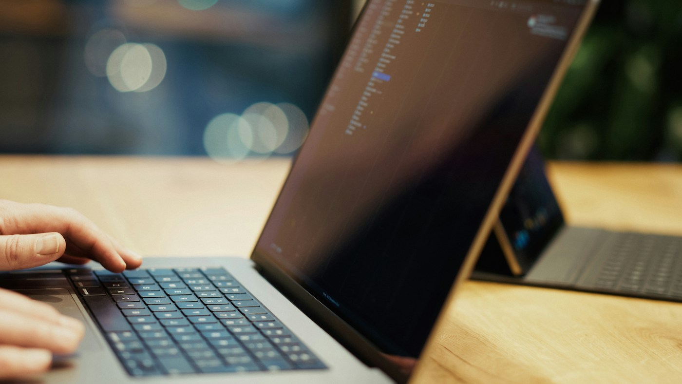 Una persona escribiendo en una computadora portátil sobre una mesa de madera