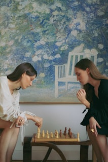 Two women playing a game of chess in front of a painting