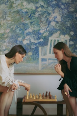 Two women playing a game of chess in front of a painting