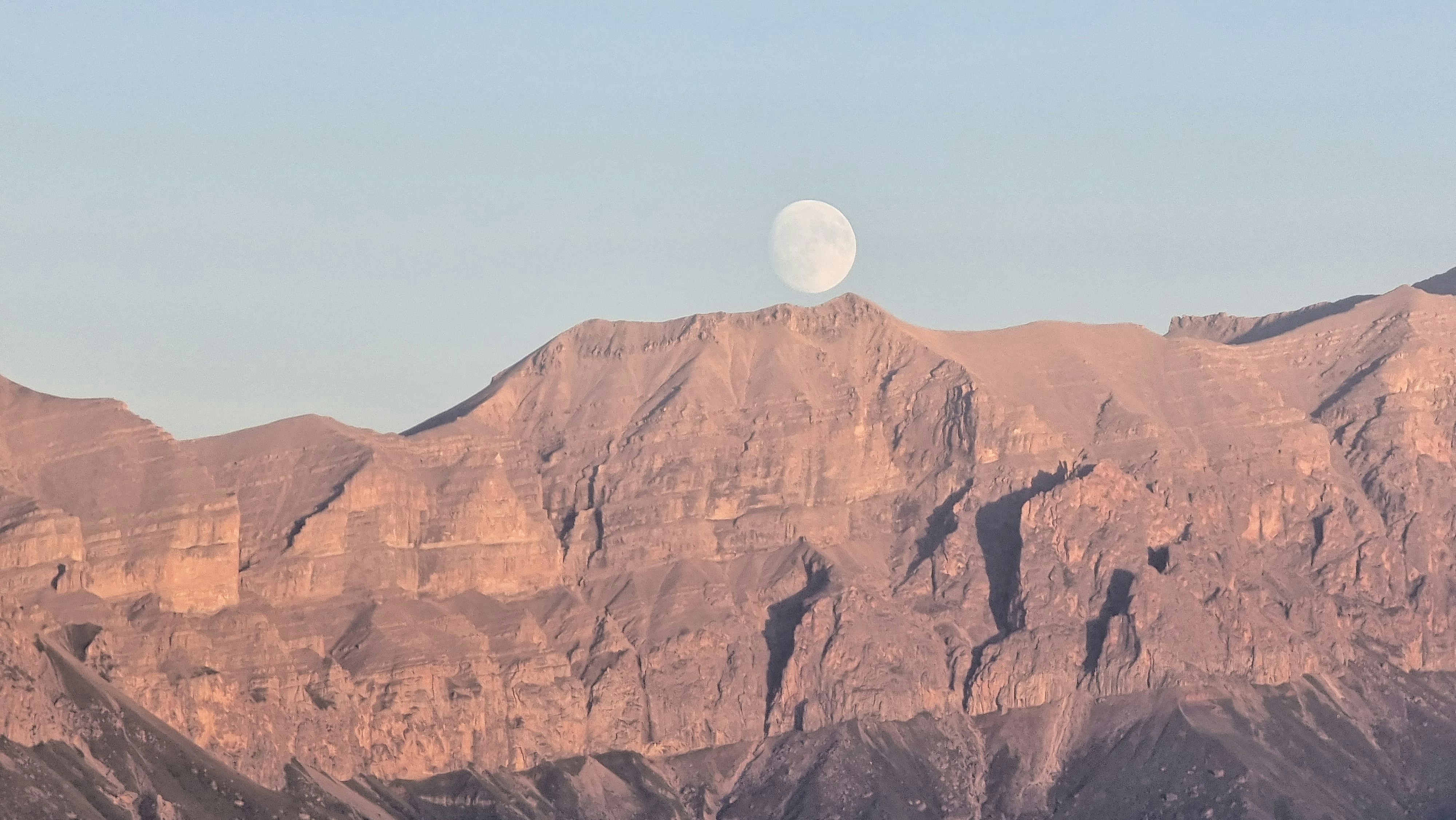 A view of a mountain range with a half moon in the sky