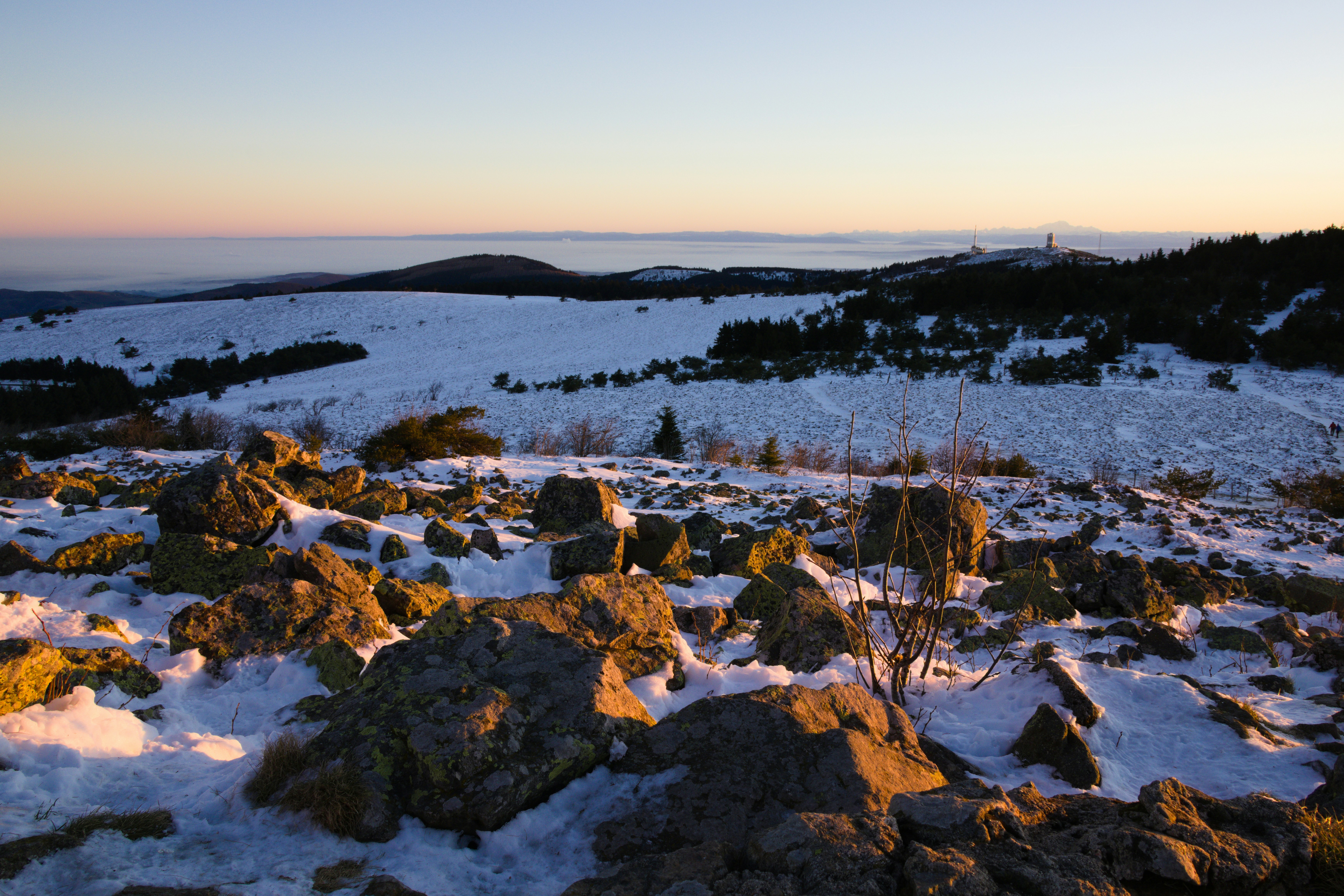 A snow covered field with rocks and a body of water in the distance