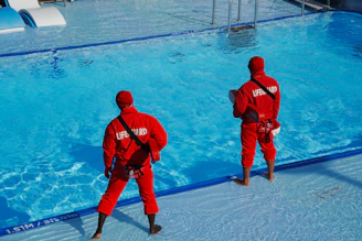 Two men in red suits standing in front of a swimming pool