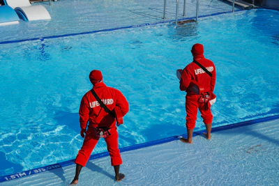 Two men in red suits standing in front of a swimming pool
