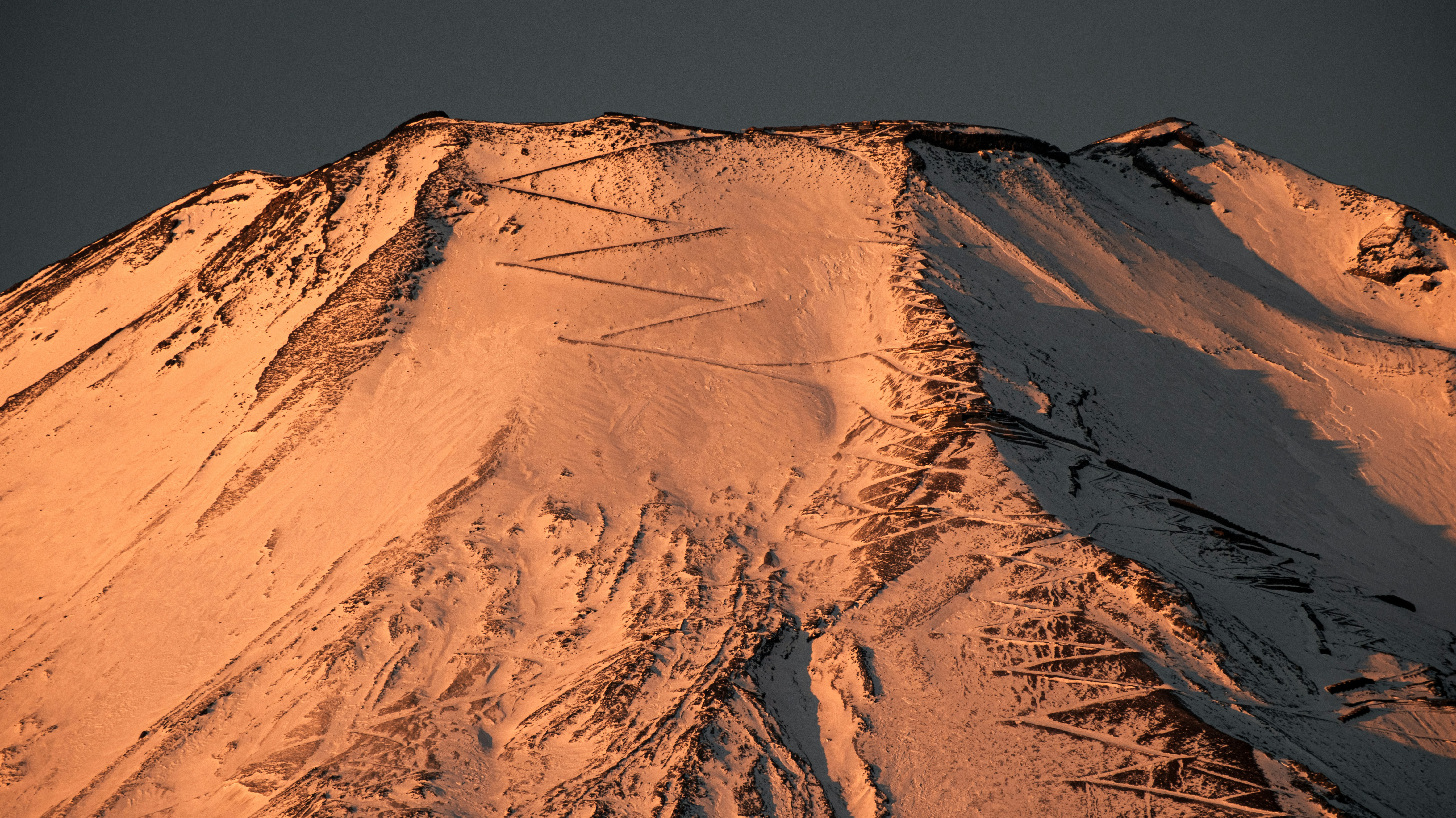 A very tall mountain covered in snow under a cloudy sky
