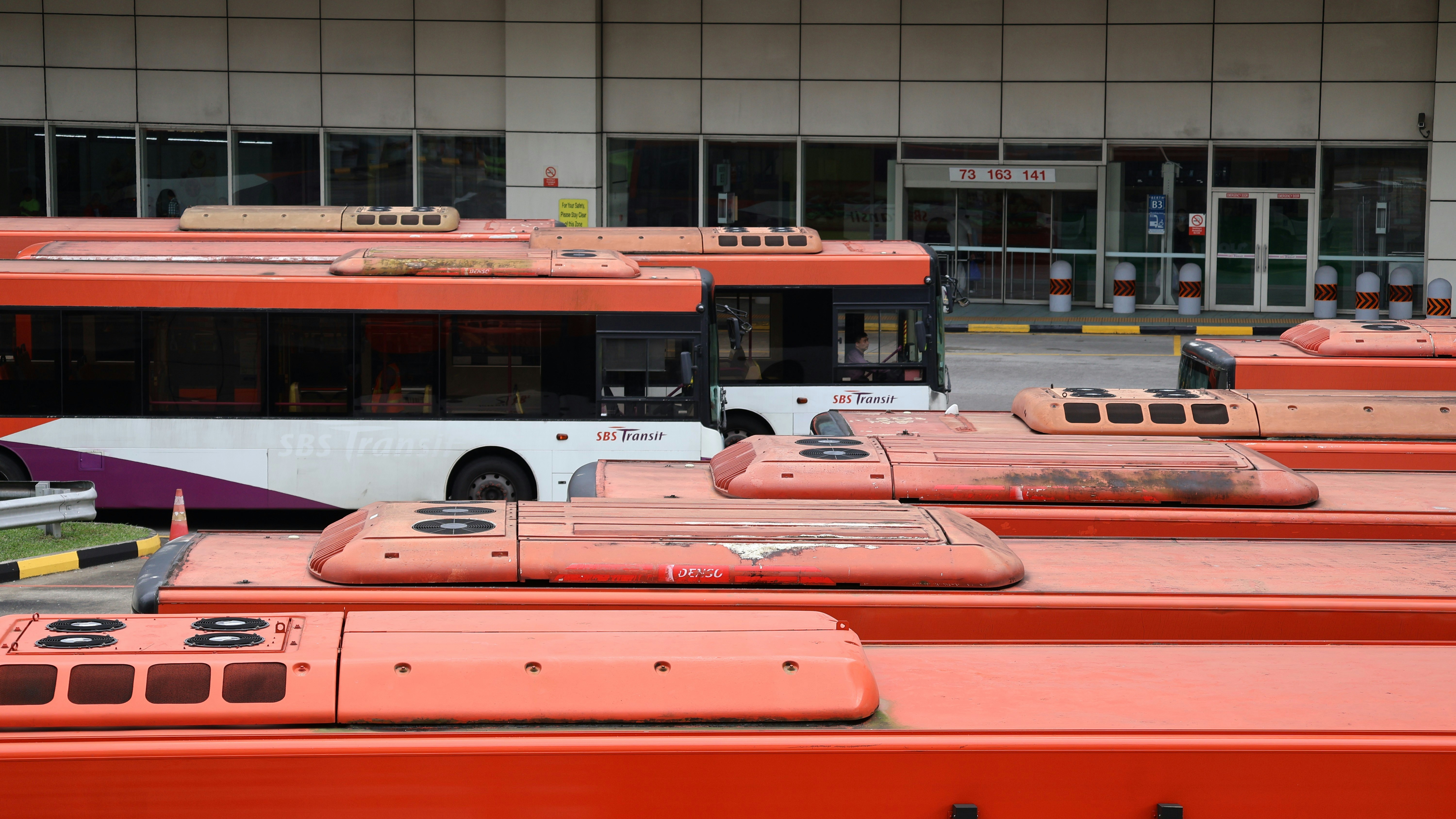 A row of orange buses parked in front of a building